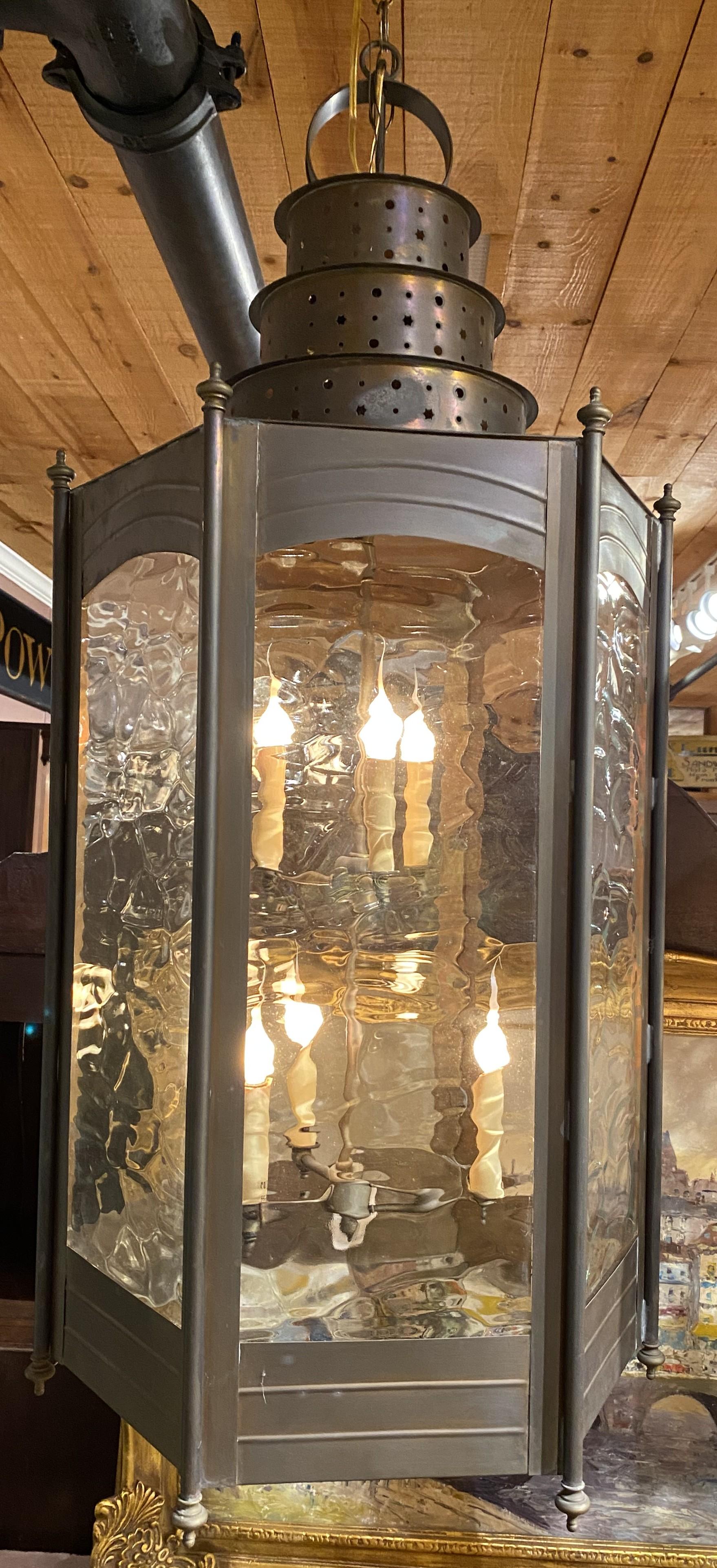 Una bella coppia di grandi lanterne o lampadari a sei luci in metallo con pannelli in vetro ondulato. La coppia è cablata per essere utilizzata su una credenza o un tavolo, ma può anche essere appesa. Sembrano fatti di rame o stagno e hanno una