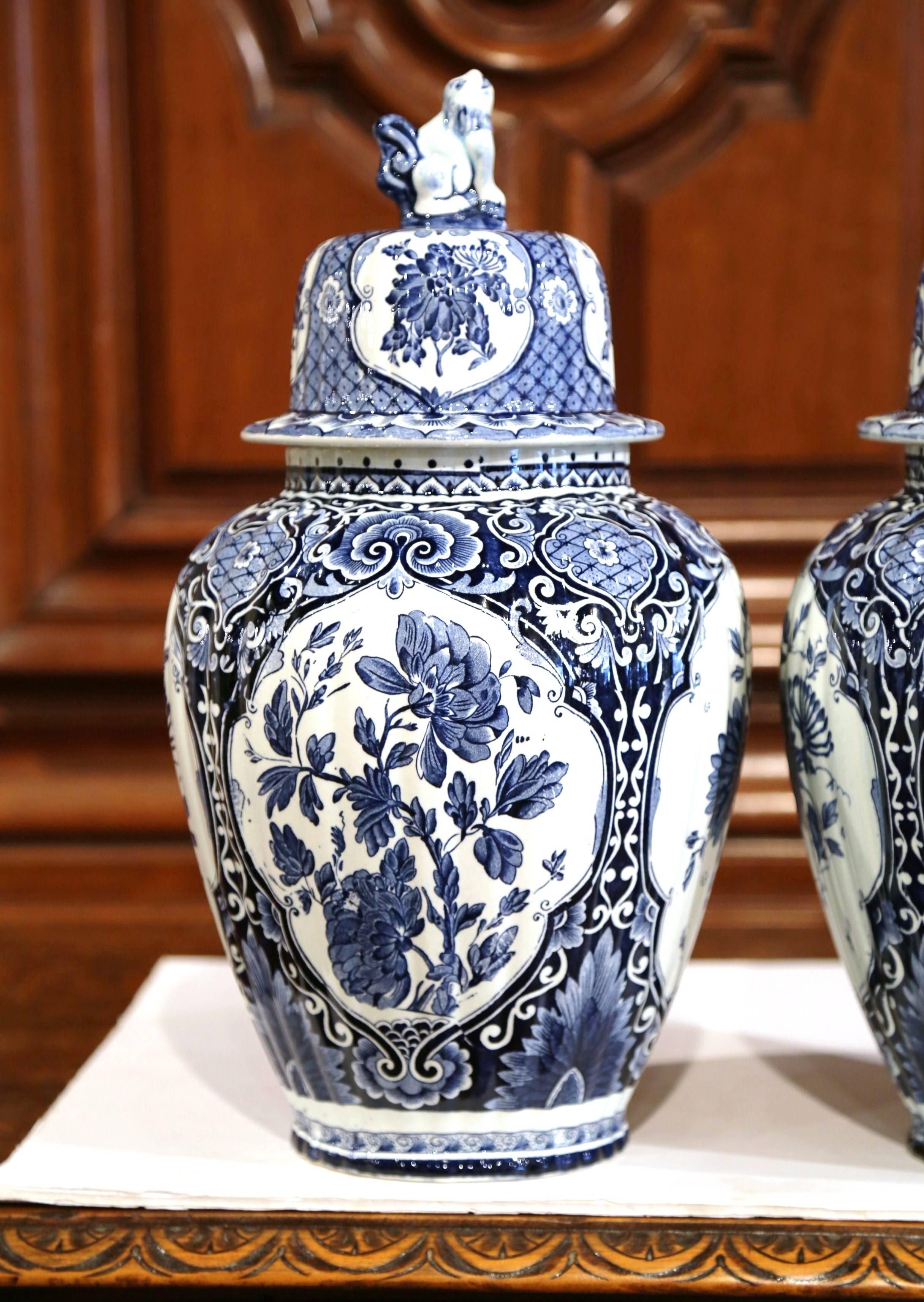 This large and elegant pair of vintage ceramic ginger jars was created in Holland, circa 1950. The faience potiches feature hand-painted medallions with Classic Dutch flowers and foliage. The traditional blue and white jars have a dome lid
