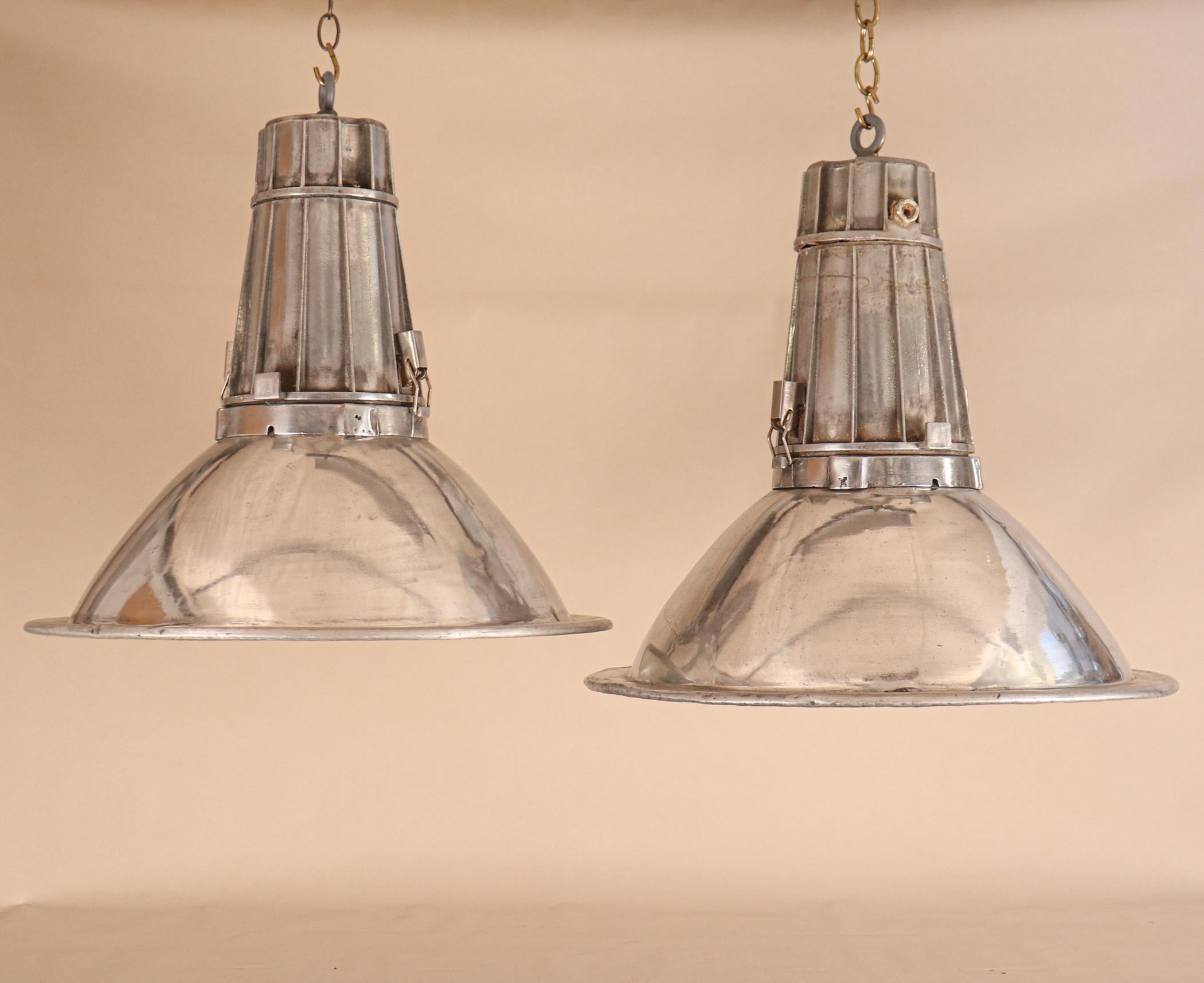 A very cool pair of aluminum industrial pendant lights, circa 1960. These midcentury floodlights have a clean, sleek form and an impactful size. They have been newly re-wired with porcelain sockets and the reflectors/lenses unclip to change a