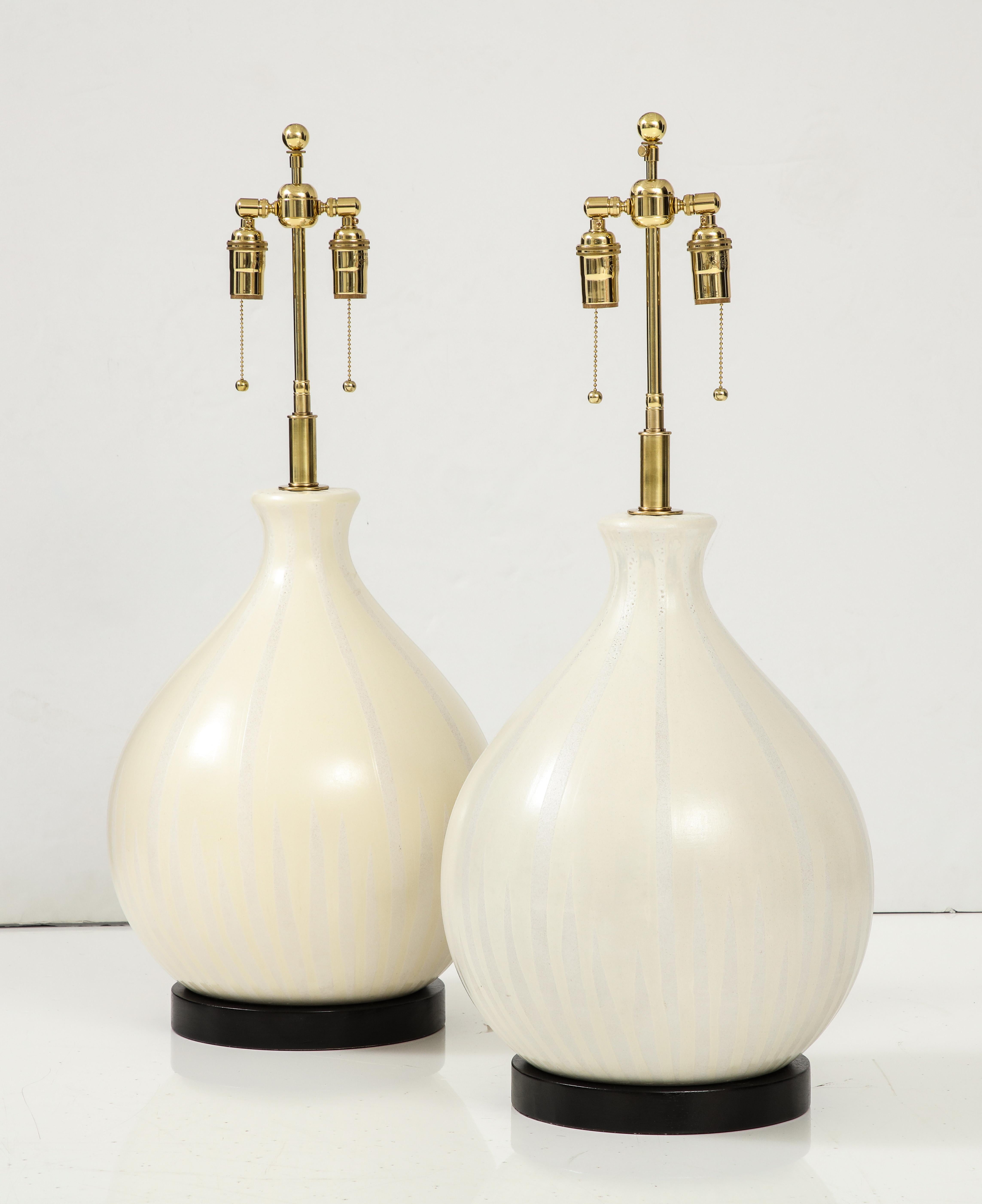 Wonderful pair of large Mid-Century Modern  balloon shaped ceramic lamps.
The Ivory glazed ceramic lamp bodies have a striped pattern and sit on black finished wooden bases.
They have been Newly rewired with adjustable Brass double clusters that