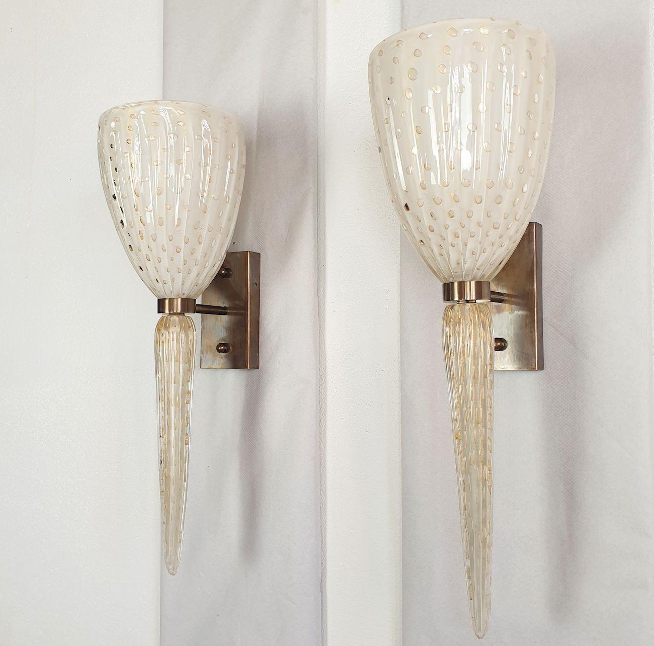 Pair of tall Neoclassical style Murano glass wall sconces, in the style of Venini, Italy 1970s.
The mid century modern sconces are in handmade Murano glass and burnished brass mounts.
The top shade is white, with an air bubbles circled by gold