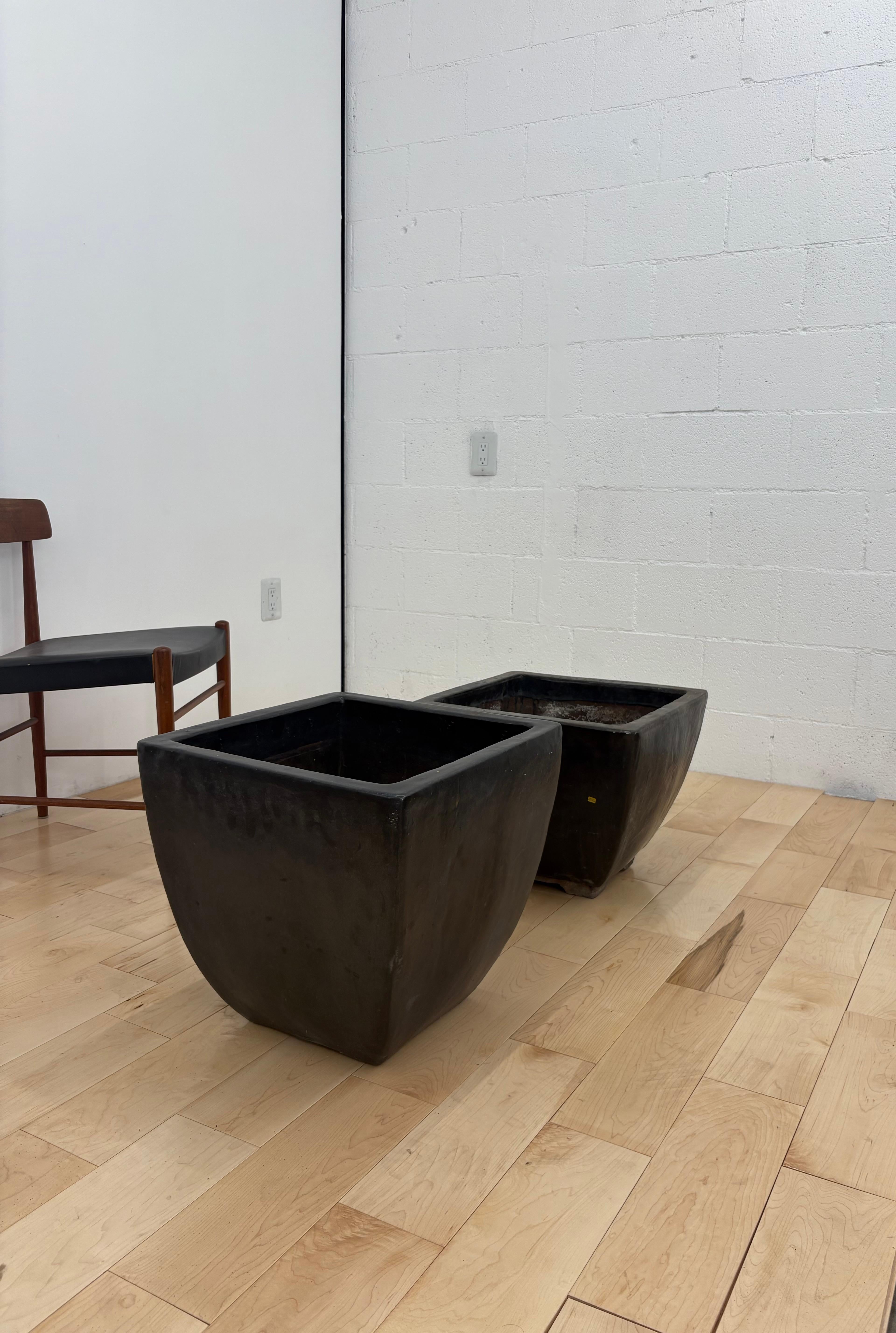 A pair of very heavy cast iron plant pots. Finished with a deep blueish black metallic glaze. 
 The pots have slightly different proportions.  
One pot is shorter and wider: 18.5” wide x 18.875” deep x 14.5”H
With a 15.875” opening

One pot is