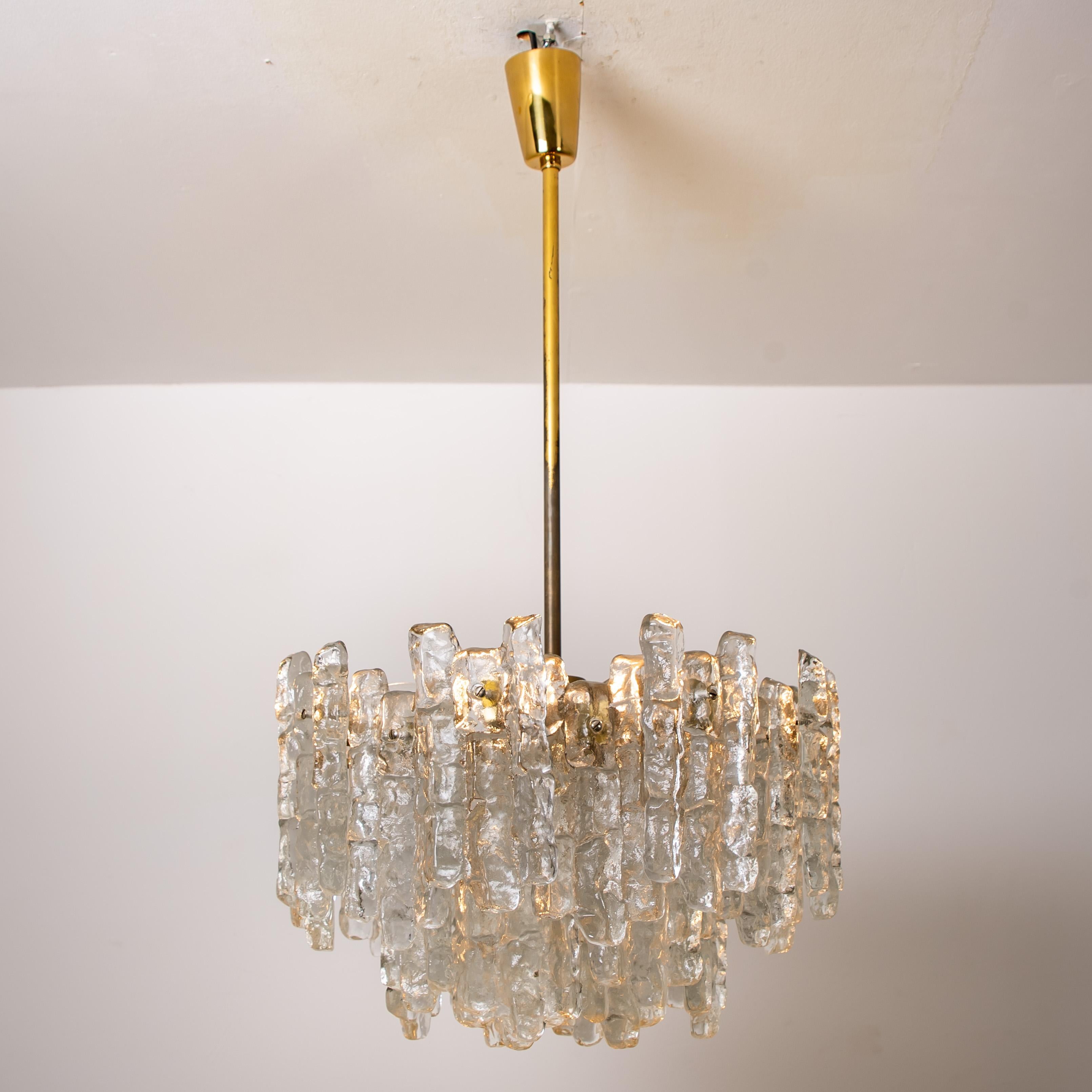 Questo lampadario moderno in ottone spazzolato, prodotto da Kalmar Austria negli anni '70, ha otto prese E27 e tre strati di 28 lastre di vetro massiccio di ghiaccio testurizzato che pendono da esso. Questi lampadari unici non funzionano solo come