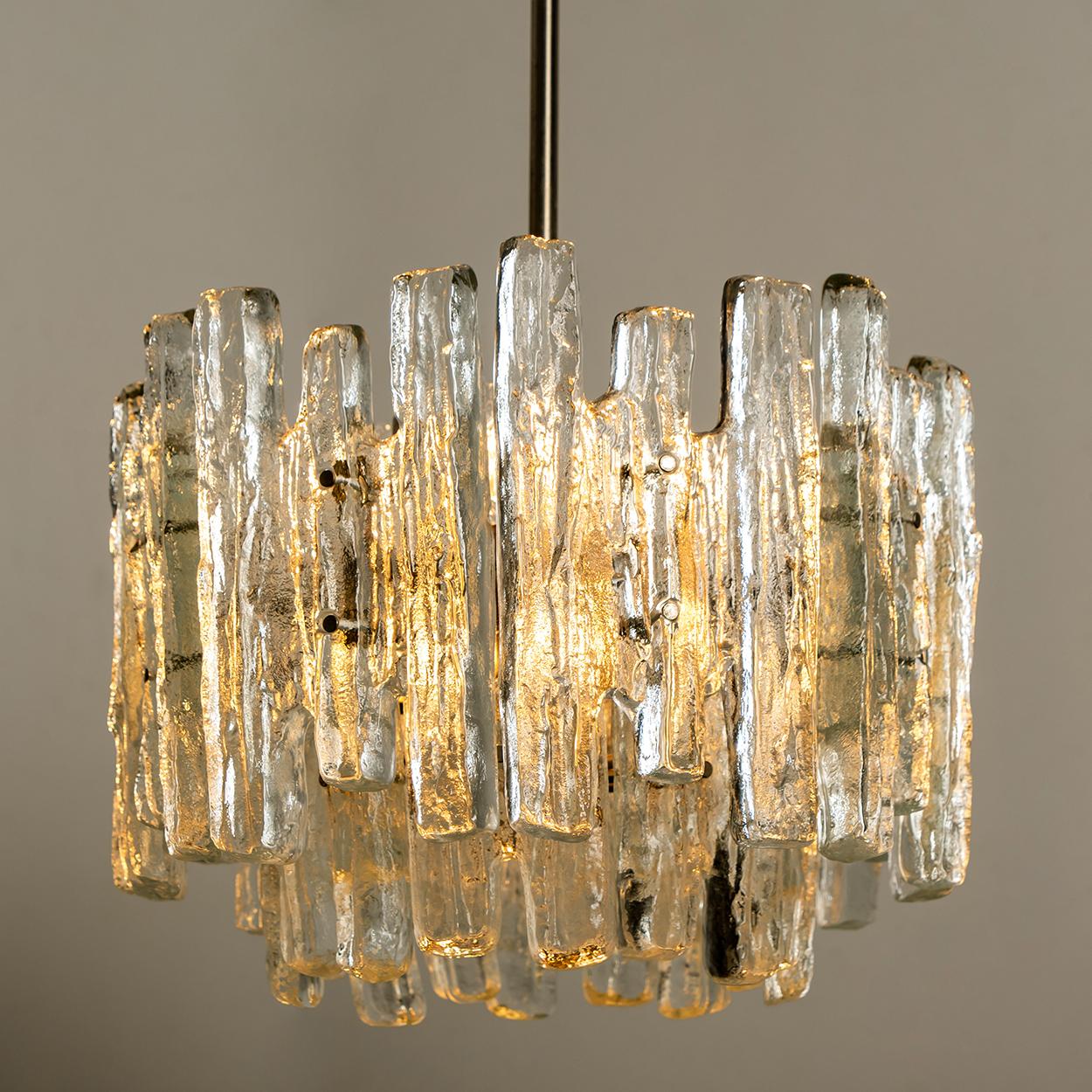 This modern chrome brushed chandeliers, manufactured by Kalmar Austria in the 1970s, have eight E27 sockets and three layers of 18 textured solid ice glass sheets dangling from it. This unique chandeliers are not only functioning as light source but
