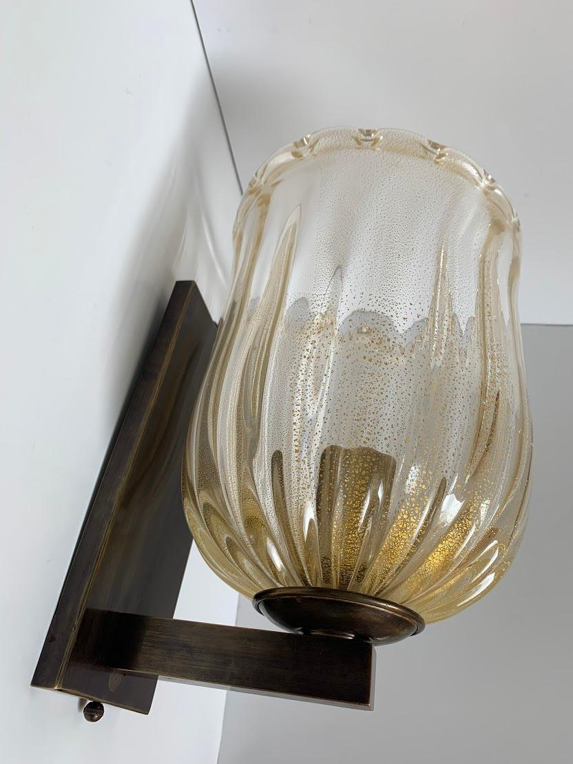 Pair of Murano sconces with real  gold fleck mouth blown glass hurricane,All brass hardware  with medium Antique acid patina . They are a little heavy and will need to be packed well for safe shipping . A quote can be given at time of sale with your