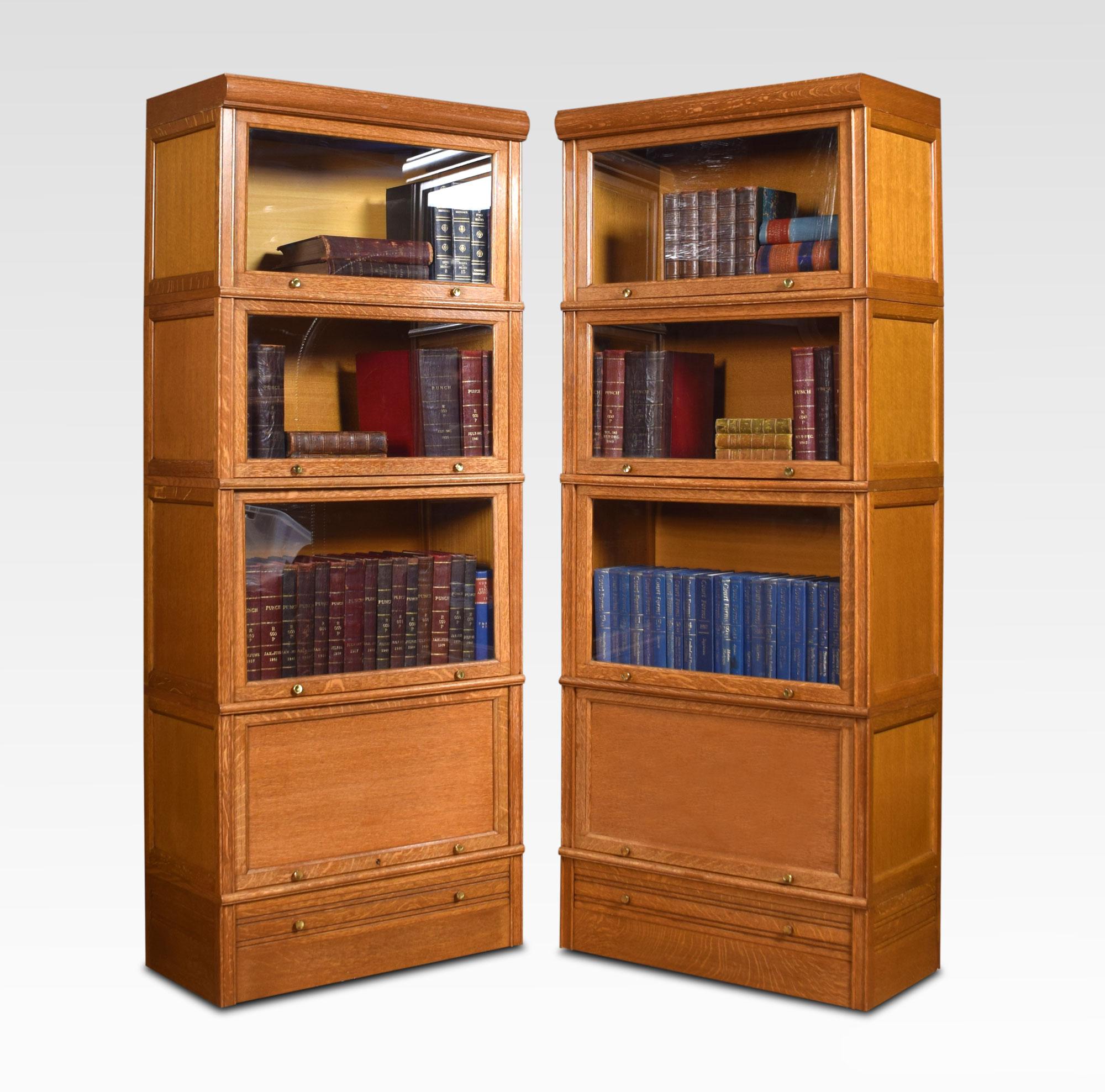 Pair of oak sectional bookcases. The moulded top above three glazed door sections fitted having paneled sides and brass knobs, the bottom sections having oak paneled doors one section fitted with shelved interior. To the base fitted with a single
