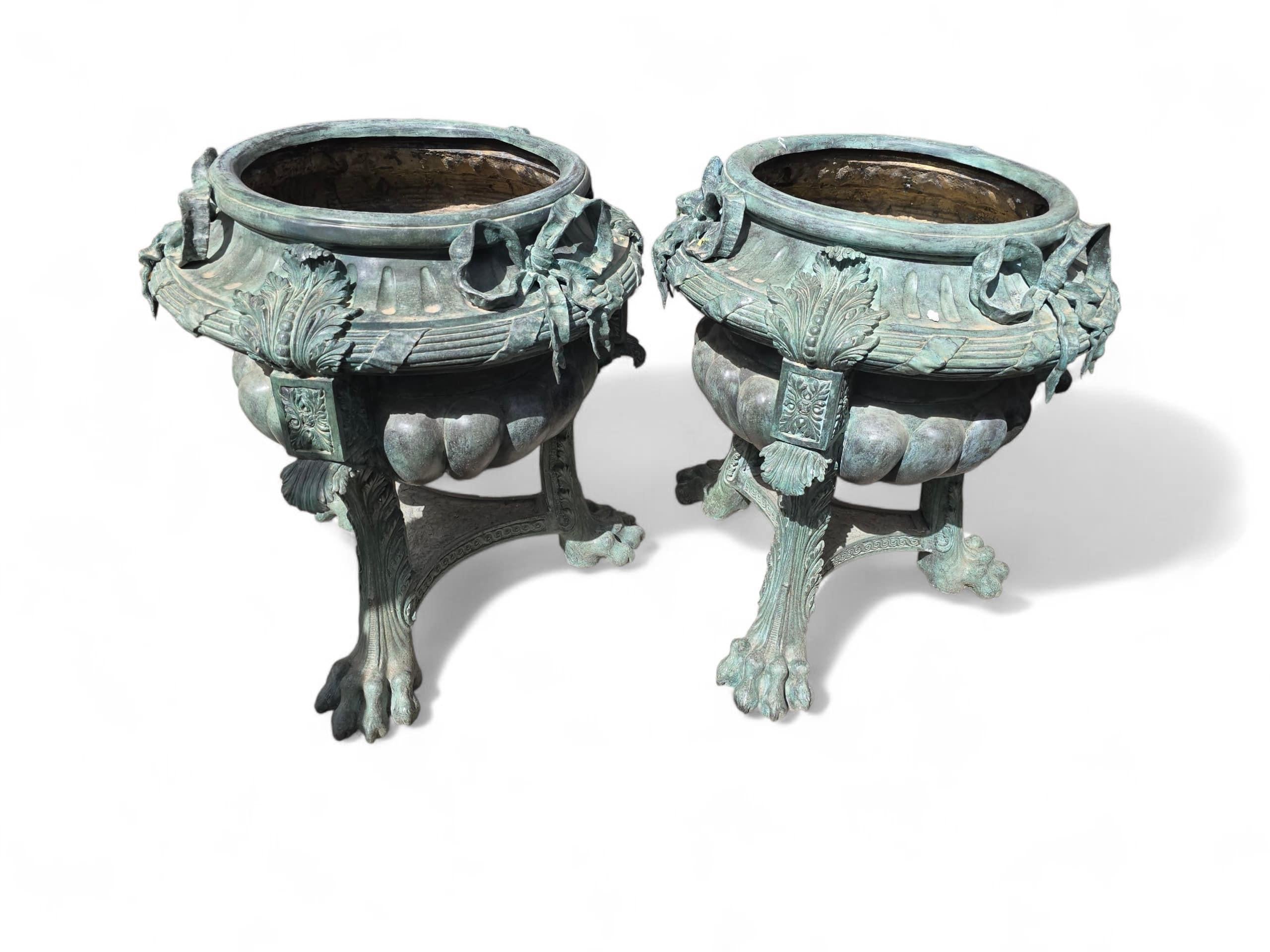 Elegant and imposing pair of large bronze planters made in the 1980s, featuring intricate floral decoration and a rich green patina. Each planter rests on finely sculpted lion paw feet, adding a classical and regal touch to their bold