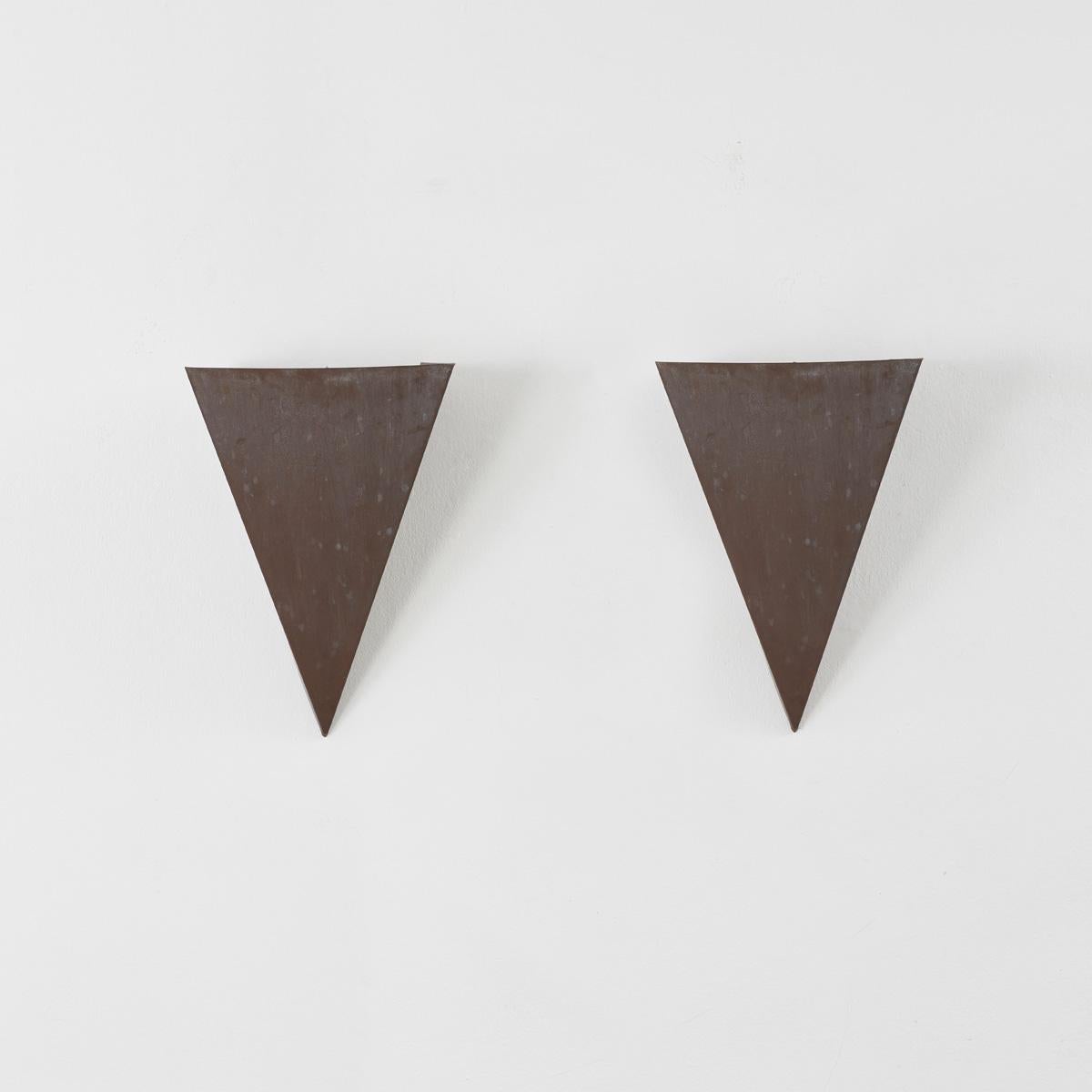 A pair of angular steel wall sconces, made by a metalworker from a sheet of steel bent at harsh angles to create a triangular shape. In turn this silhouette casts dynamic shapes, guiding the light and shadows across the wall.