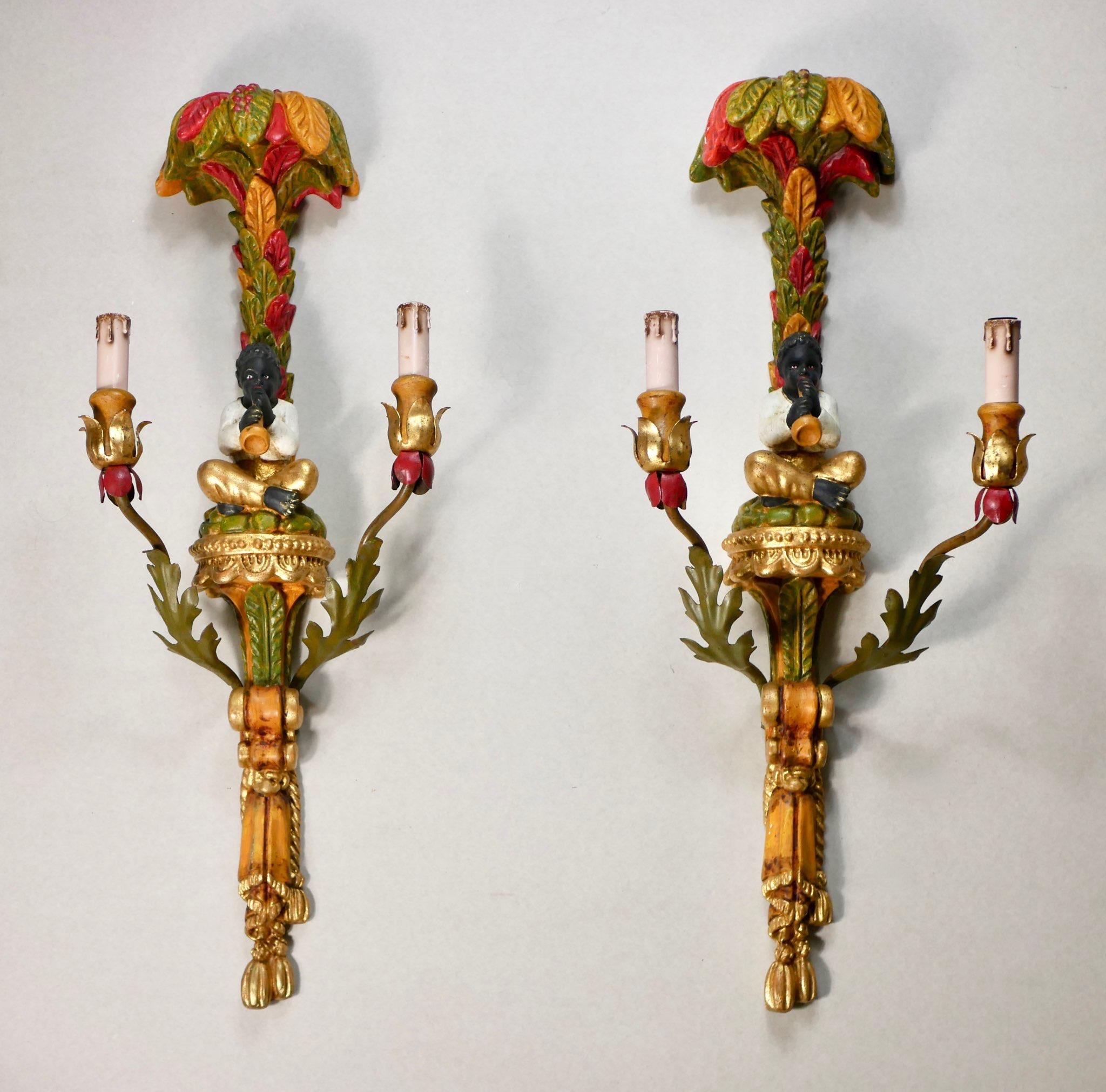 Stunning pair of large polychrome hand carved wood sconces, in the style of the Venetian creations of the 18th century, made in Italy in the early 1920s. 
Representing a Nubian playing flute under a palm tree, they feature vibrant colors, gilded
