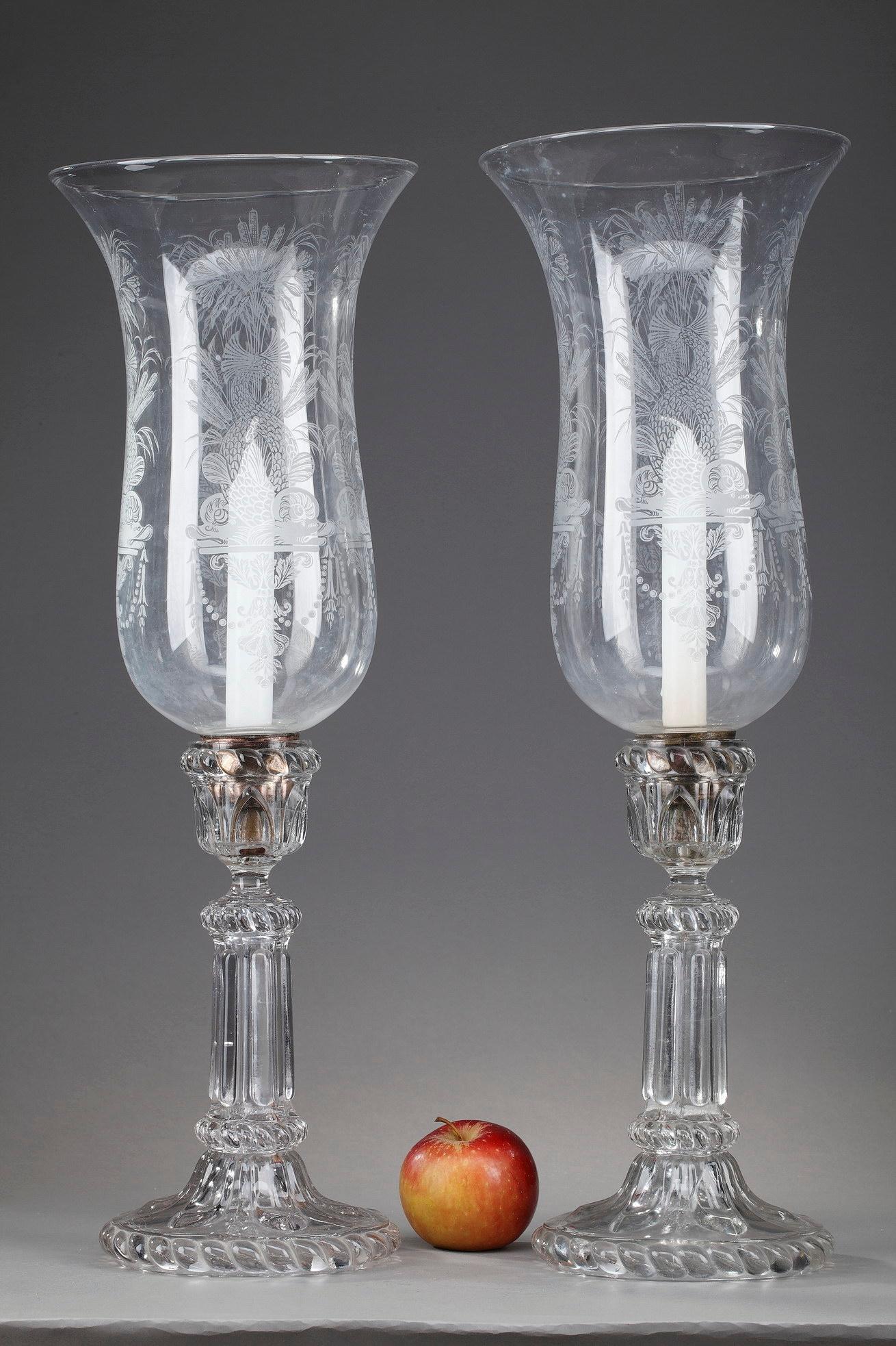 This monumentally-sized pair of crystal candleholders was executed by the French glassmaker Portieux (1705-2012). Crafted in the early 20th century, they are intricately engraved with dolphins, vases and foliage. Each lamp is resting on a fluded