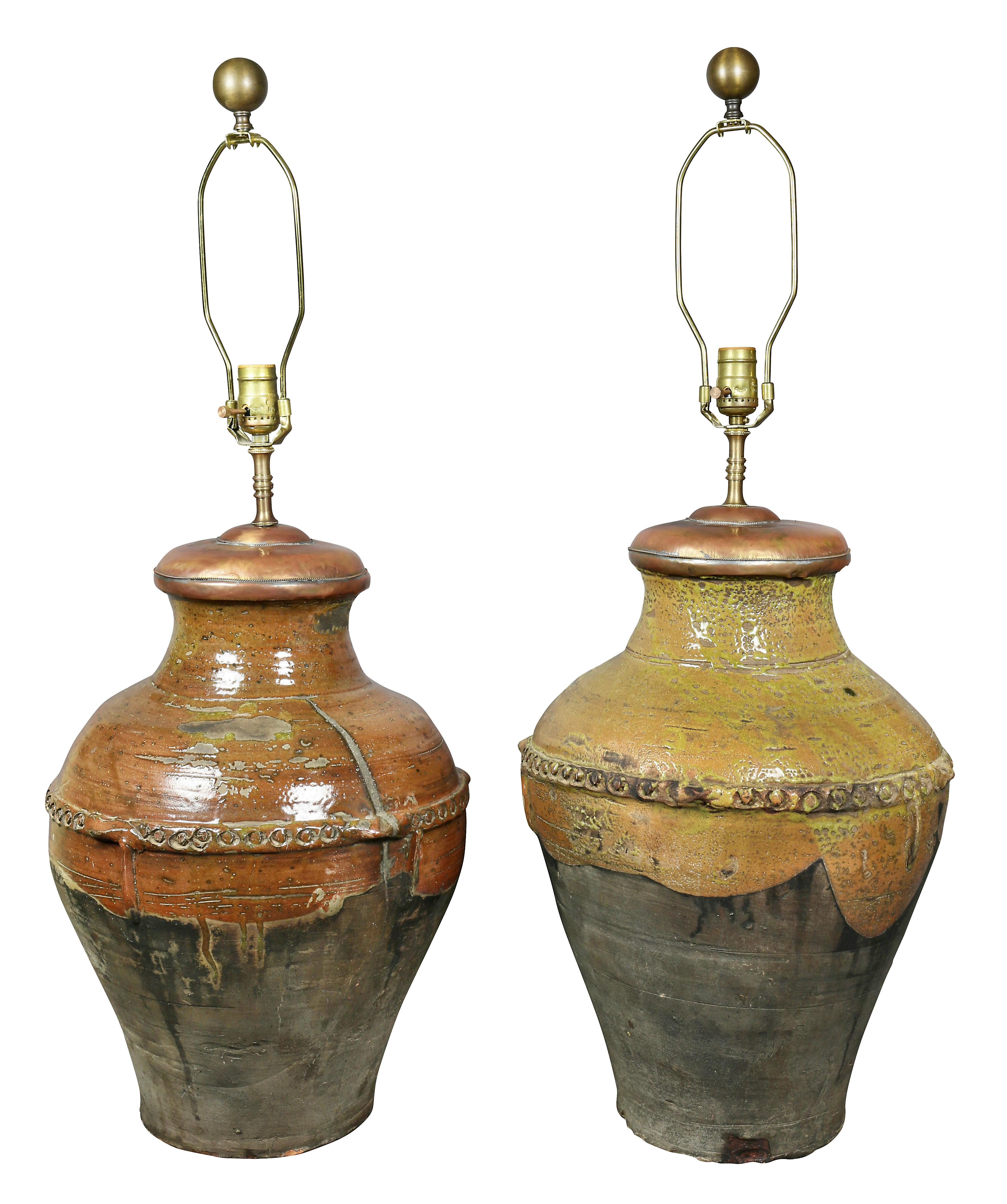 Each with a single socket with copper cover for jar lid, baluster form partially glazed with applied decoration, includes shades.
Provenance: Michael D Dingman.
 