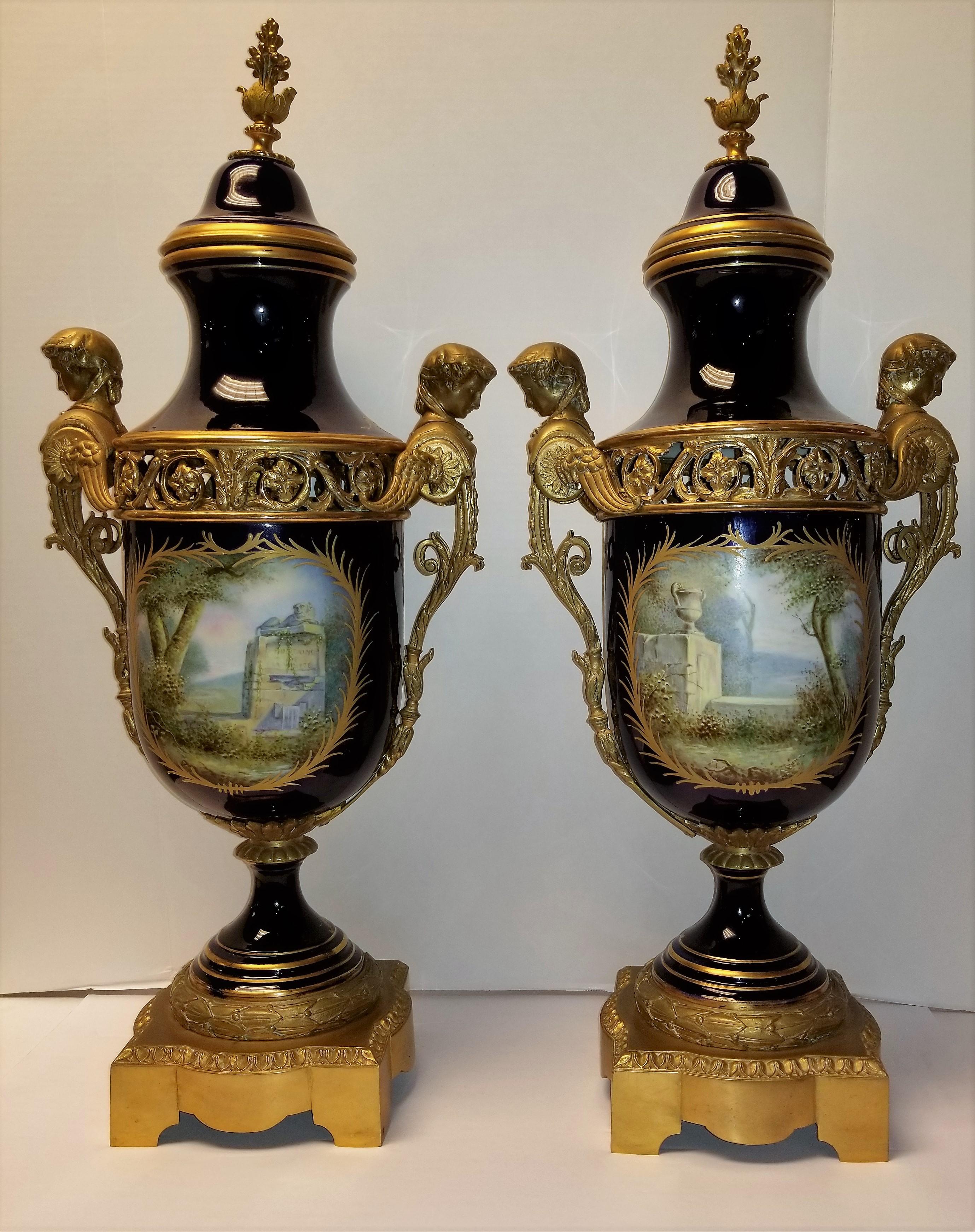 A magnificent and large pair of 19th century French Royal cobalt blue Sèvres Porcelain and bronze mounted covered vases. Each panel is beautifully hand painted with Watteau love scenes, and further adorned with 24-karat raised gold and enamel