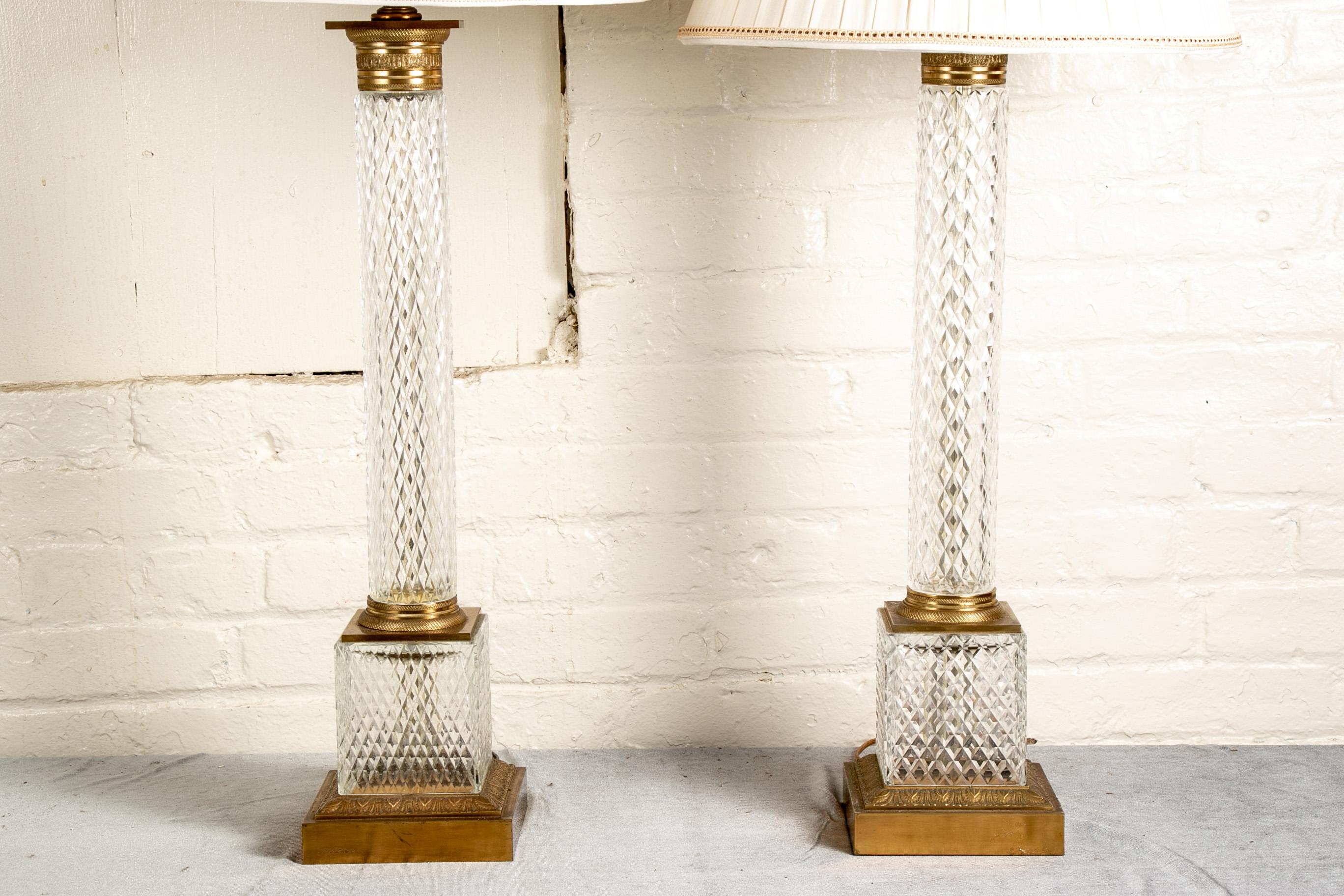 Pair of large scale cut crystal column lamps, overall cut diamond pattern columns and plinths with bronze mounts. The column collars and bases with finely cast details, the square bases with leafy bands in relief. White silk pleated