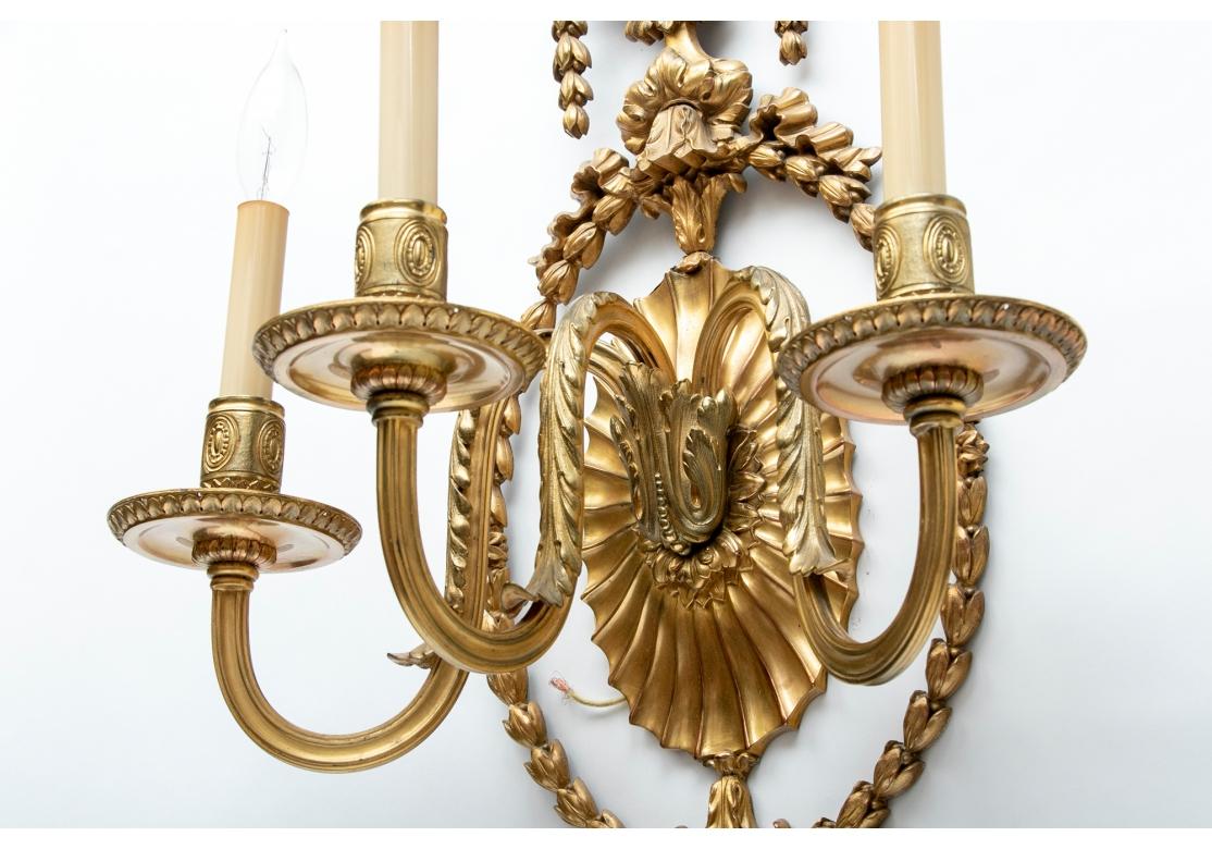 Tall finely crafted gilt metal sconces with elaborate details. The crests with palmettes on top of urns with pendant bell flowers. Openwork bell flower ovals with bows at the tops and bottoms, and pendant oak leaf and acorn terminals. The scrolled
