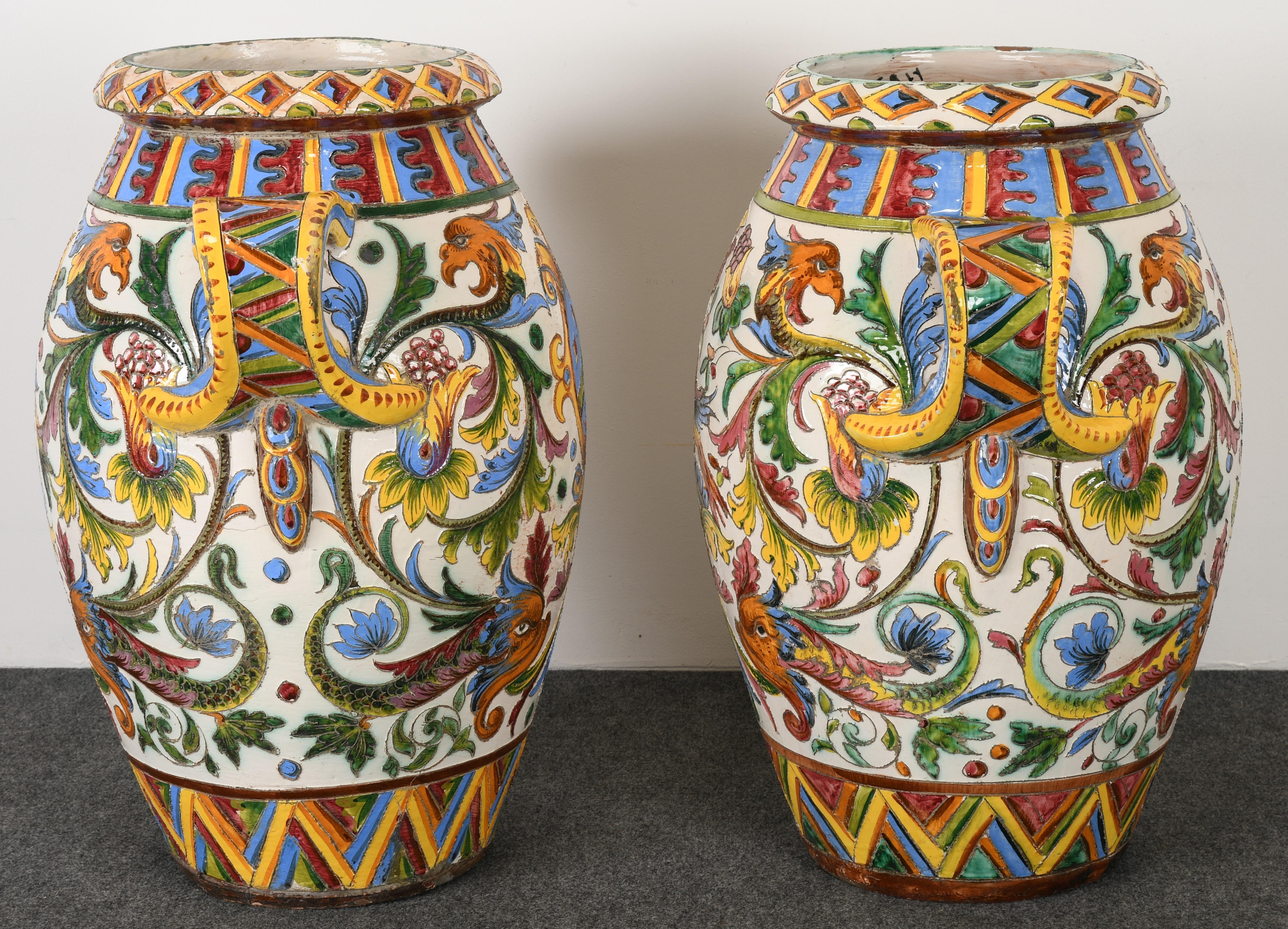 A stately pair of large-scale Italian Majolica Terracotta Urns. These one-of-a-kind Earthenware vases are extremely colorful and striking with hand-painted Sgraffito work of vibrant depictions of griffins, dolphins, and a coat of arms Painted 