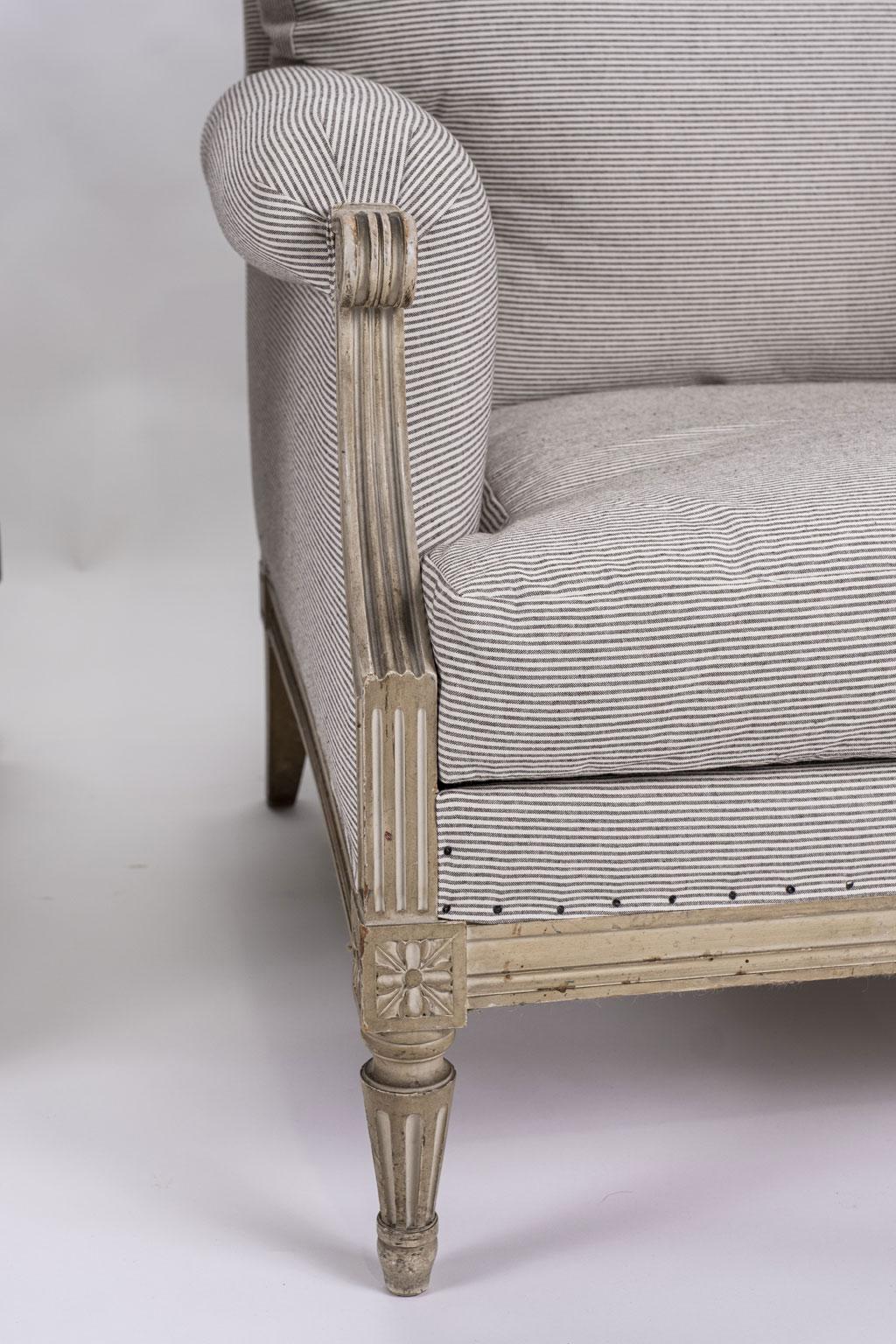 Pair of large scale painted bergère armchairs in ticking: Louis XVI style armchairs (circa 1910) with nice, large comfortable proportions. Painted in light gray and off-white. Newly upholstered in white and gray pinstriped ticking. Sturdy and