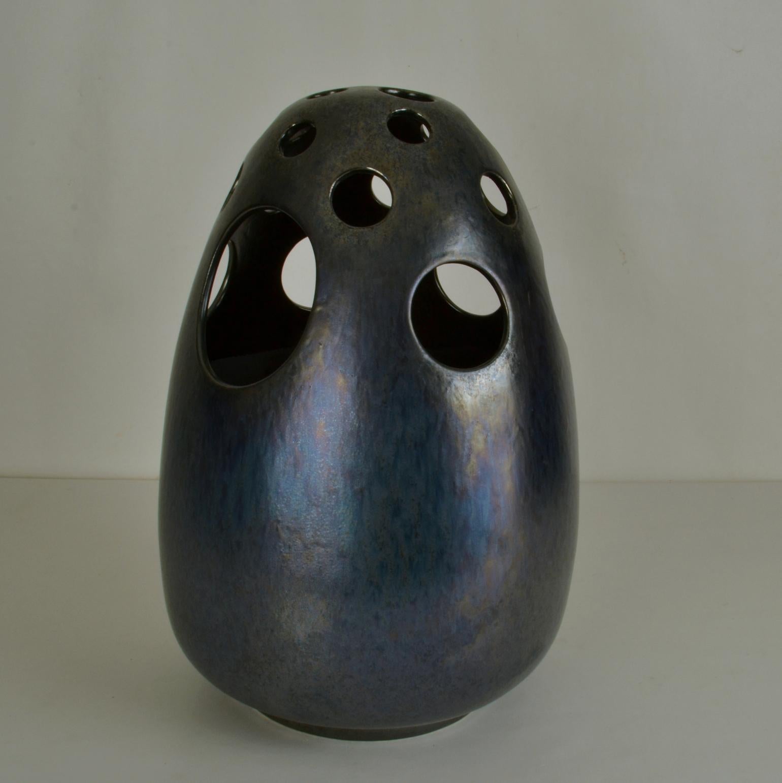 Large decorative vases are sculpted into an egg form. They are perforated with holes cover at the the top of the vessels alternating into a series of medium to large holes almost half way down the vase. Over the surface the glaze is applied ranging