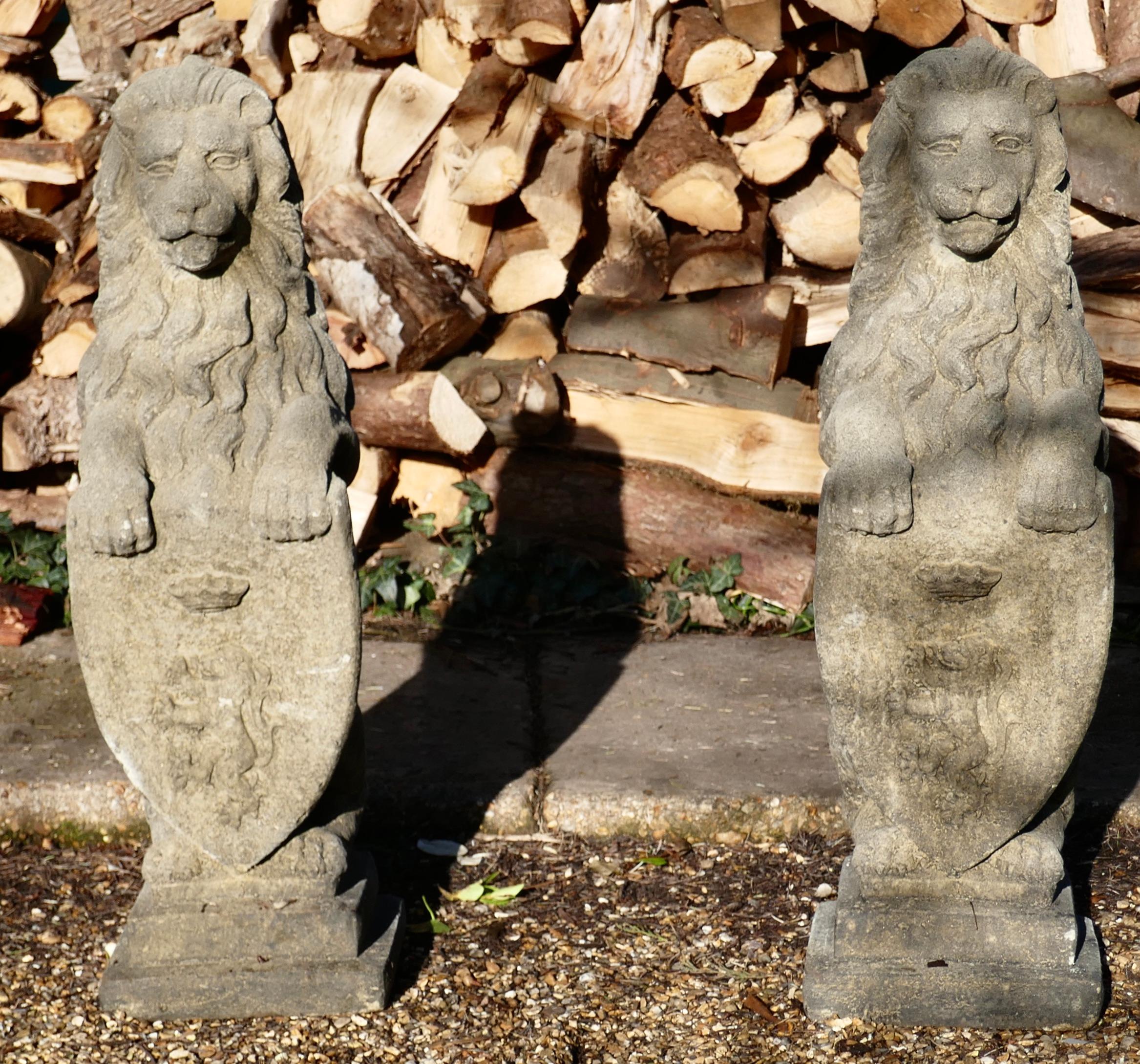 Pair of Large Sculptures of English Stone Heraldic Lions

These are weathered Statues of Male Lions they sit proud with raised paws resting on a heraldic shield which has a coronet over a Lion Rampant 
The Lions are fully sculpted in the round