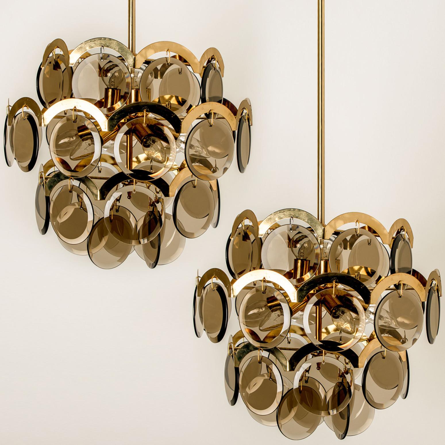 Pair of gorgeous four tiers hanging light fixture, in the style of Vistosi, Italy.
With graduated tiers of smoked round facet glass discs framed by half moon shaped brass. The chandelier is complete - no hook or glass disk is missing.

Both elegant