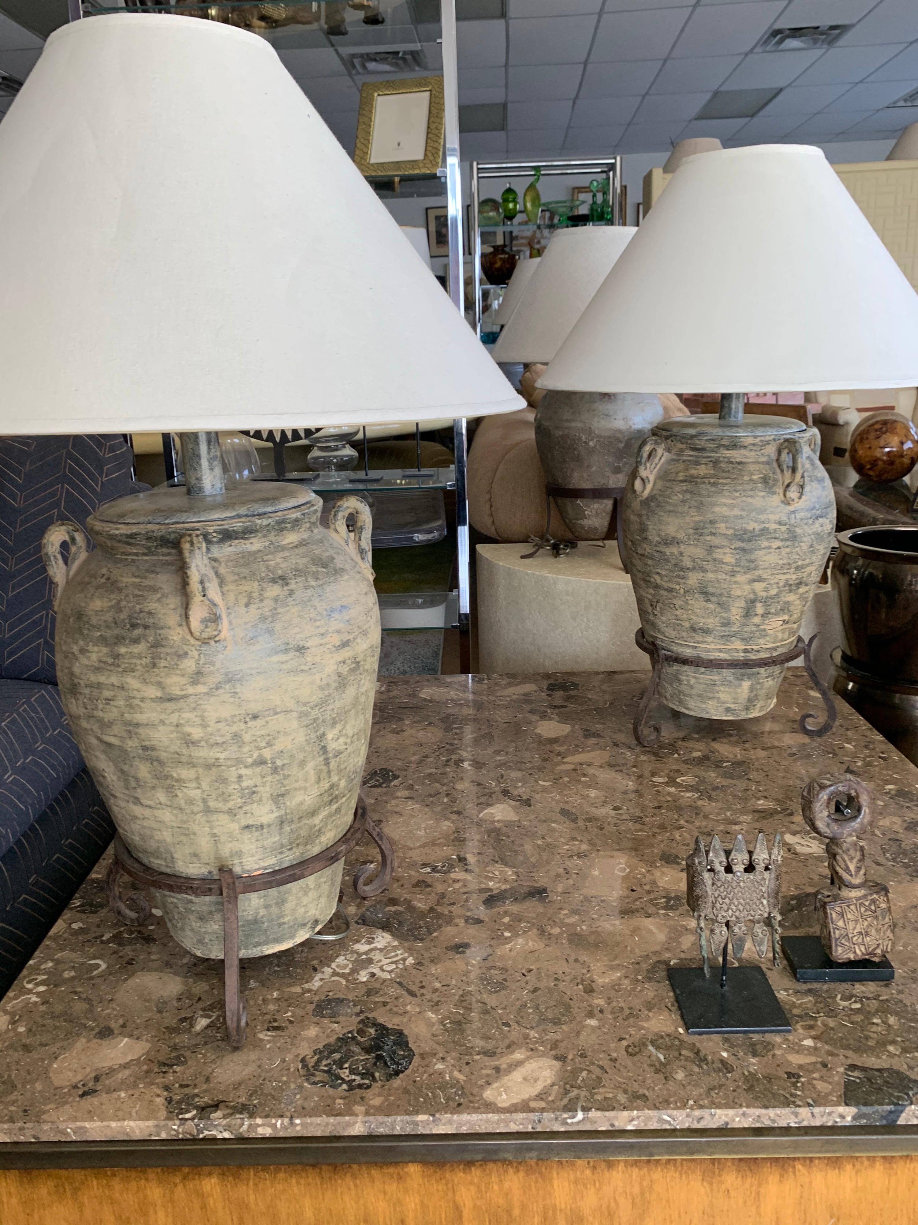 These amazing custom made living room lamps are made out of antique urns on patina iron stands. and designed by the late Steve Chase for a Vintage CC residence. Beautiful patina throughout the lamp and stems. Double sockets. Obtains original shades.