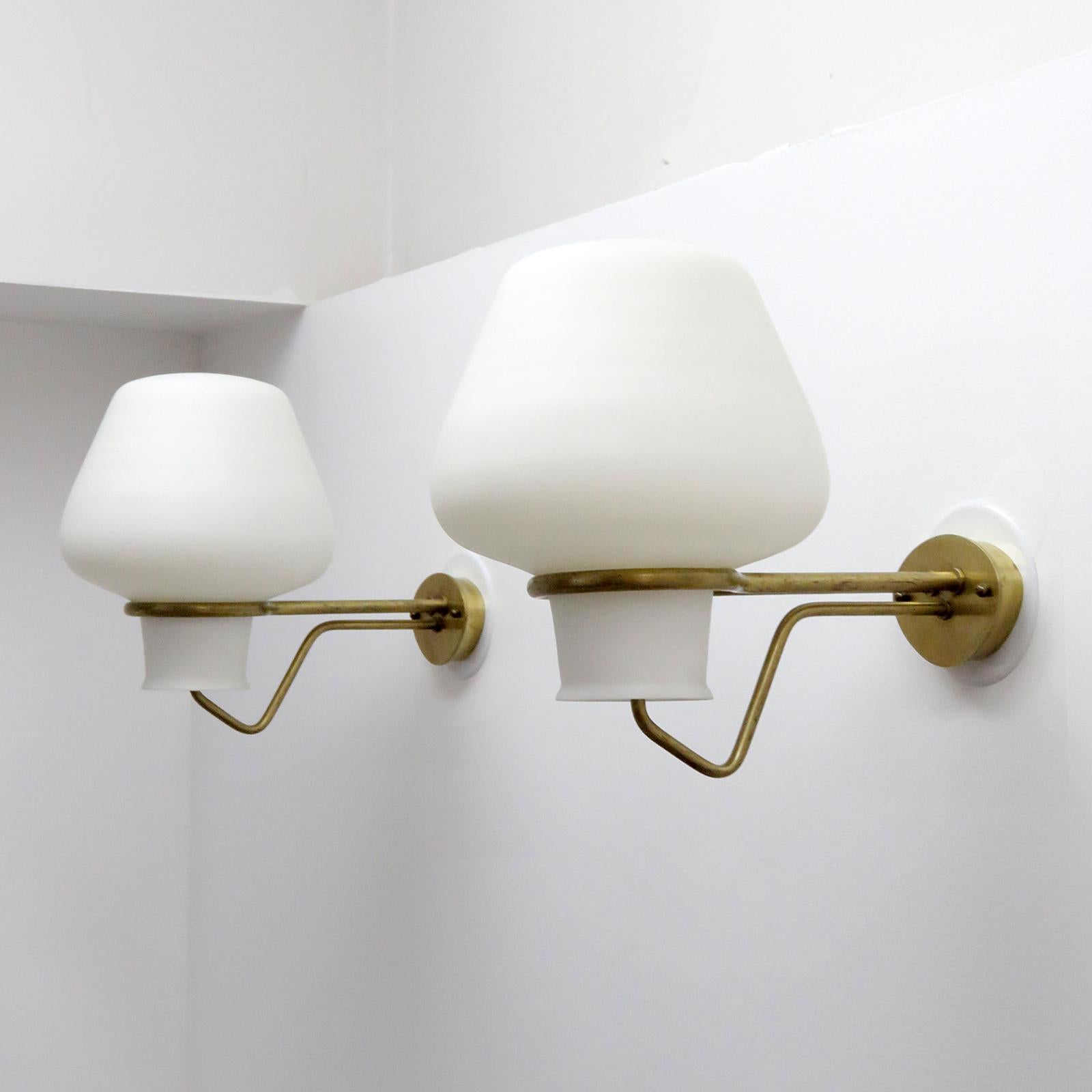 Elegant pair of large scale indoor/outdoor wall lights by Erik Gunnar Asplund for ASEA, Sweden, 1950 with matte opaline cased glass shades on minimalist brass arms.