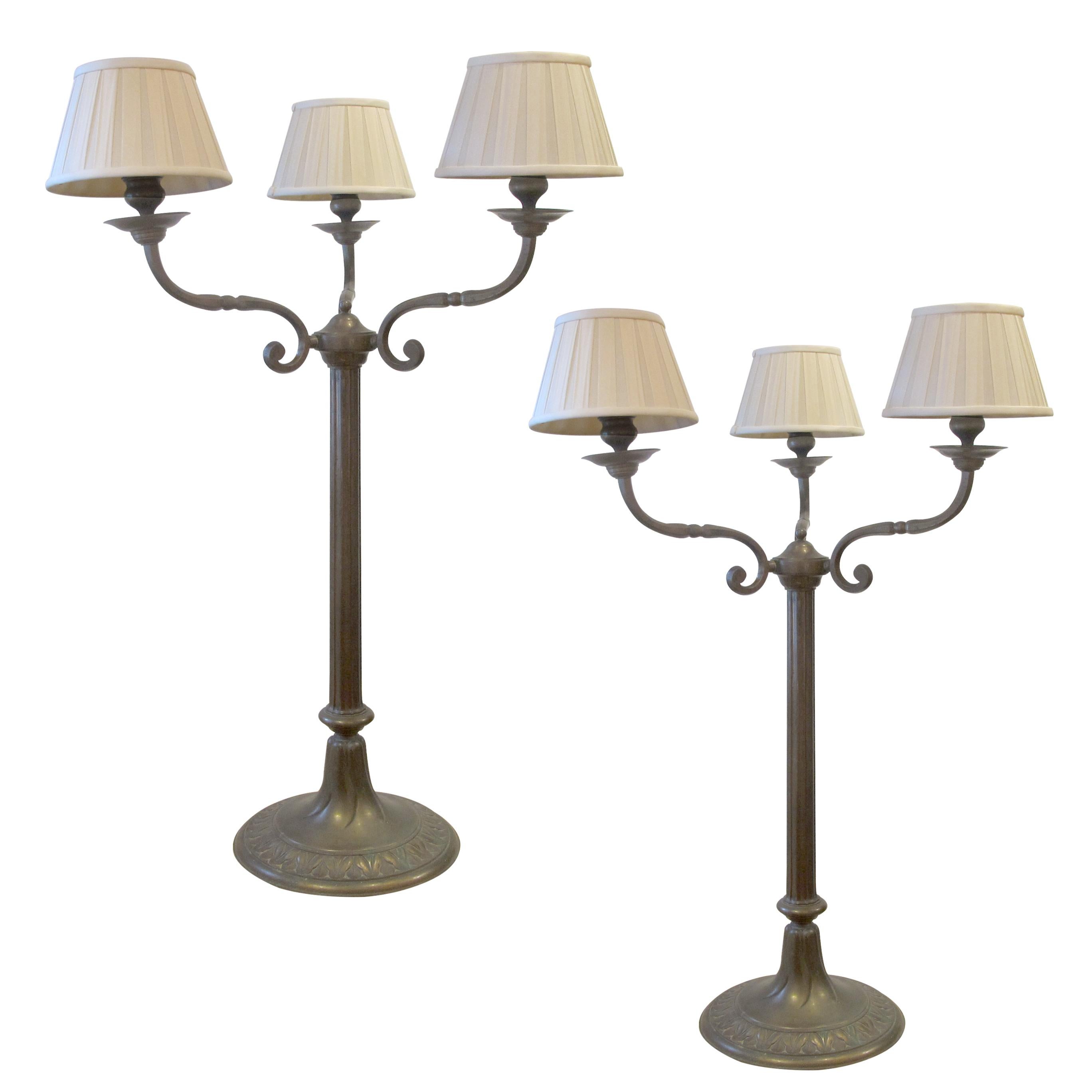 This stunning pair of large bronze table lamps, dating from around 1900, embodies the elegance of the early 20th century. Each lamp features a gracefully curved three-arm design, reminiscent of classic candelabras, supporting three lampshades with