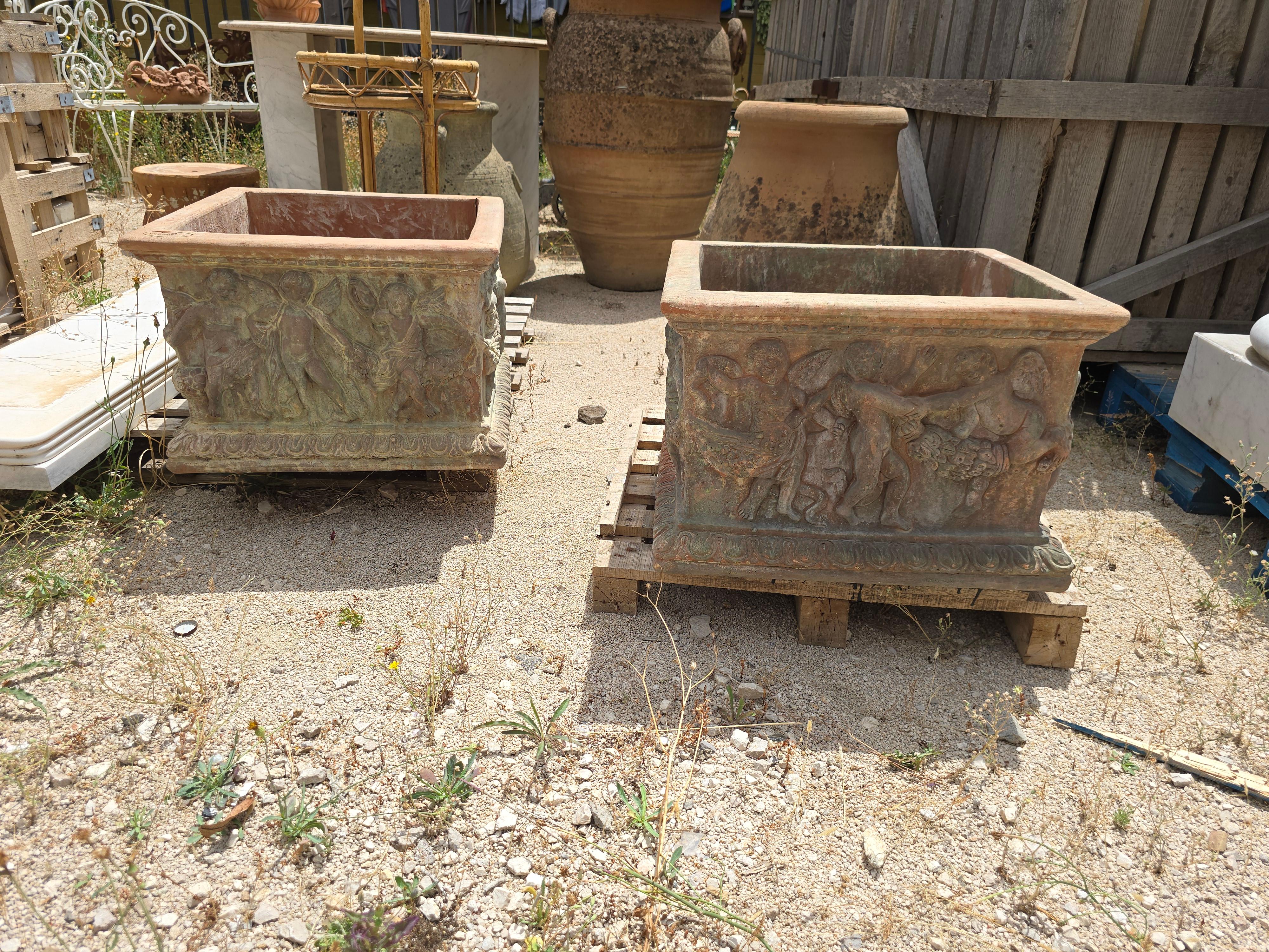 Charming pair of large square terracotta planters crafted in Tuscany, featuring decorative reliefs of playful cherubs on each side. These traditional Italian pots are made from warm, natural terracotta and exhibit classical motifs that evoke a sense