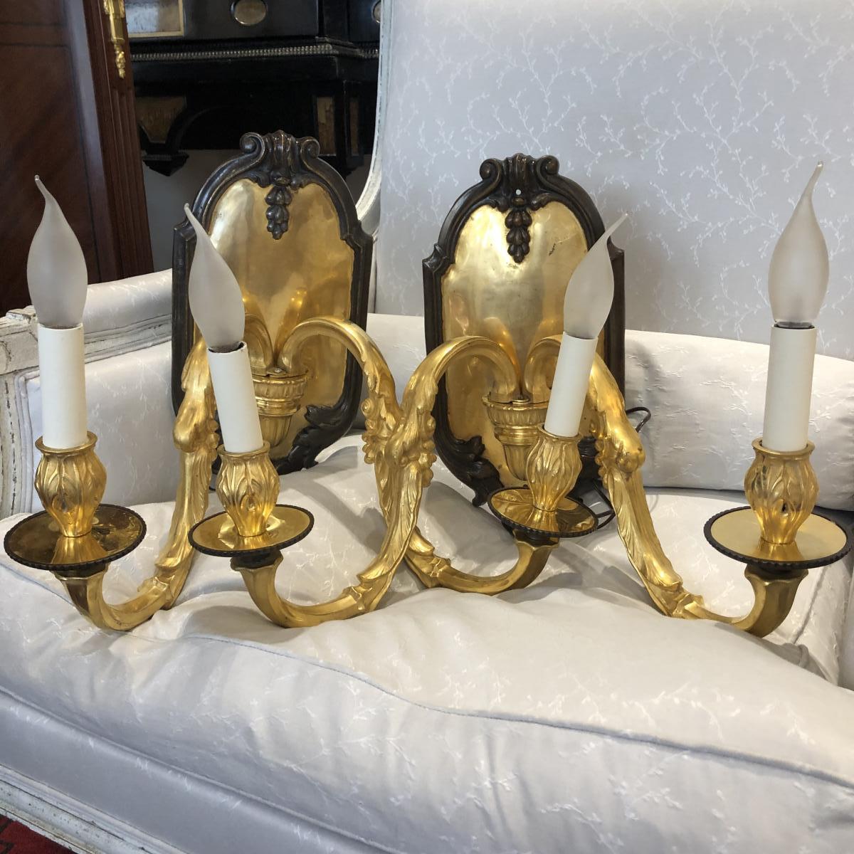 Este par de apliques de pared de estilo Luis XVI, de dos luces cada uno y 47 cm de ancho, se fabricó en Francia hacia 1900. Realizados en bronce dorado y bronce patinado marrón, ejemplifican la calidad y el refinamiento del bronce decorativo francés