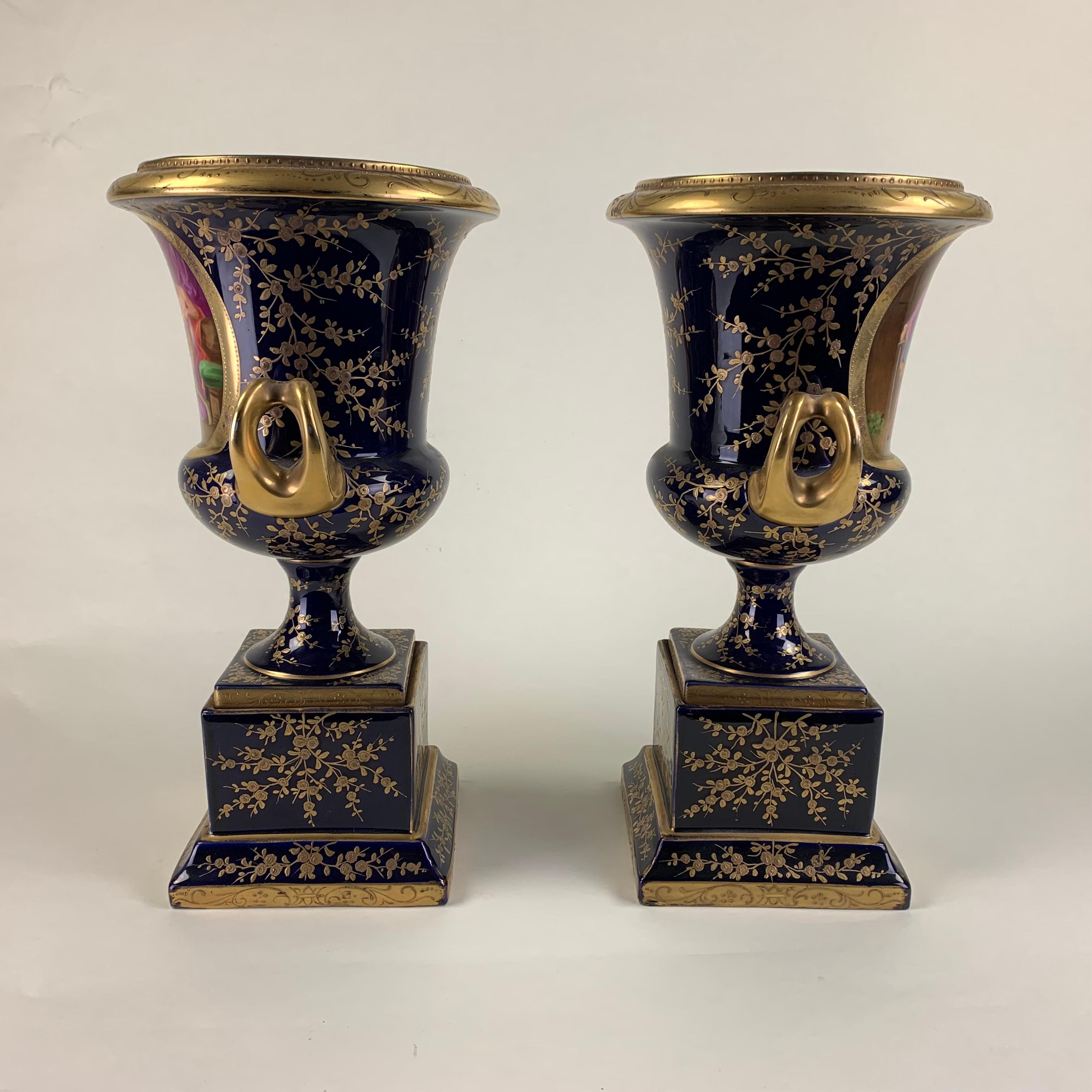 Paire de vases viennois en forme de campane, très décoratifs et imposants, décorés sur fond bleu foncé de scènes de théâtre classique dans les cartouches principaux, orientés vers l'avant, ainsi que dans les cartouches plus petits sur les