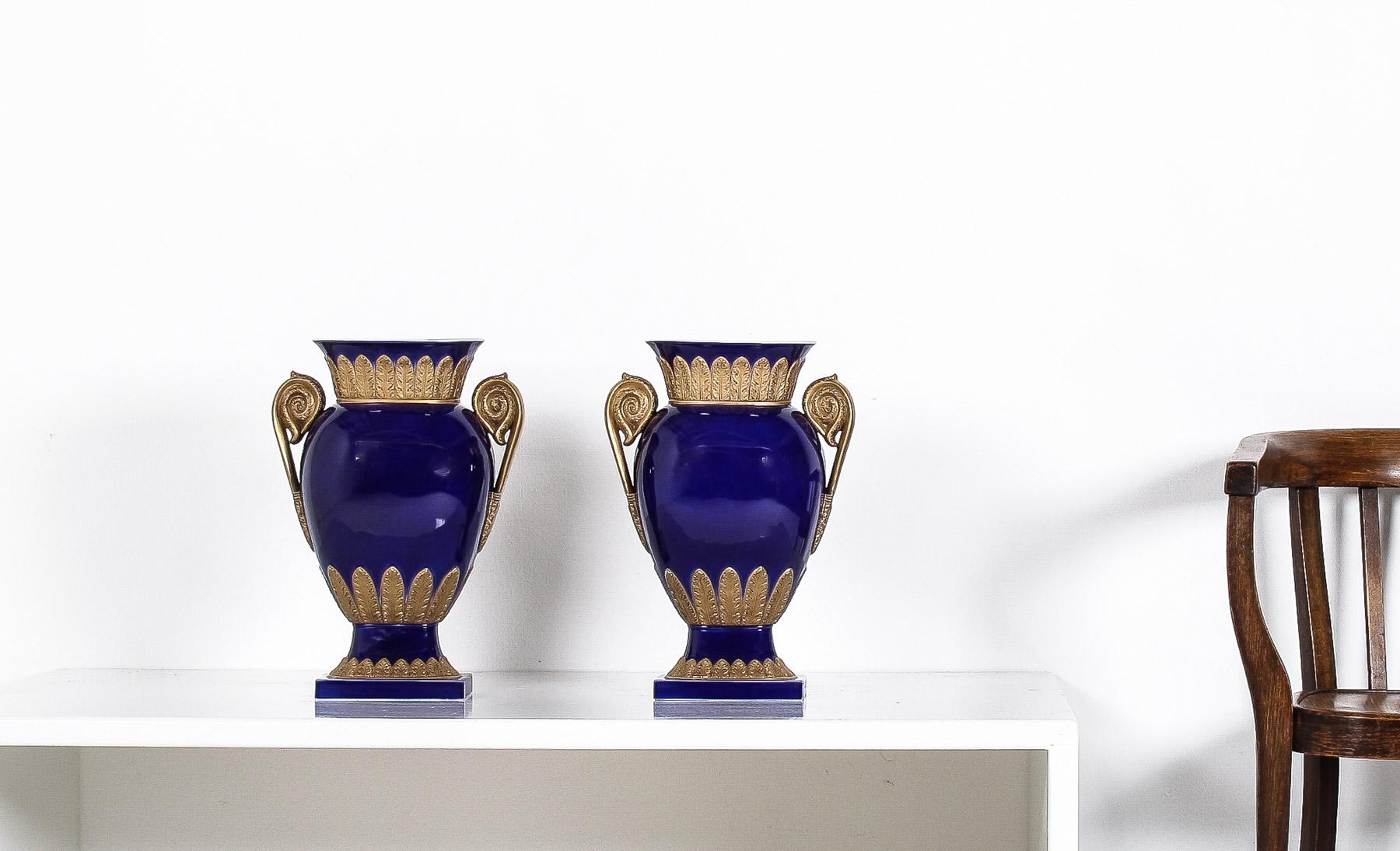 These exquisite vintage porcelain vases from the 1980s, crafted by Agostinelli, Italy and sold by Harrods, epitomize the luxurious Rococo Regency style. The vases are adorned in a striking cobalt blue, which provides a vivid backdrop for intricate