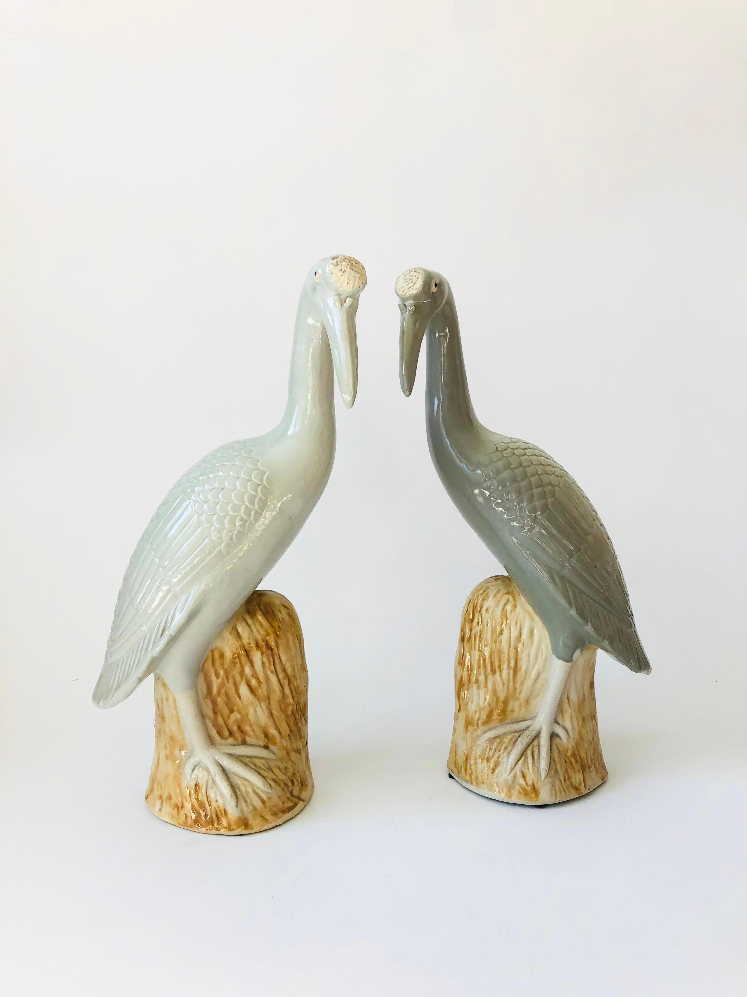 A pair of Chinese porcelain cranes. Beautiful detailed, gracefully perched on faux wood bases. Pale gray and white glazes with tan glaze to the bases. Nice large size to use as statement pieces. Each is stamped on the base by the maker. Estimated