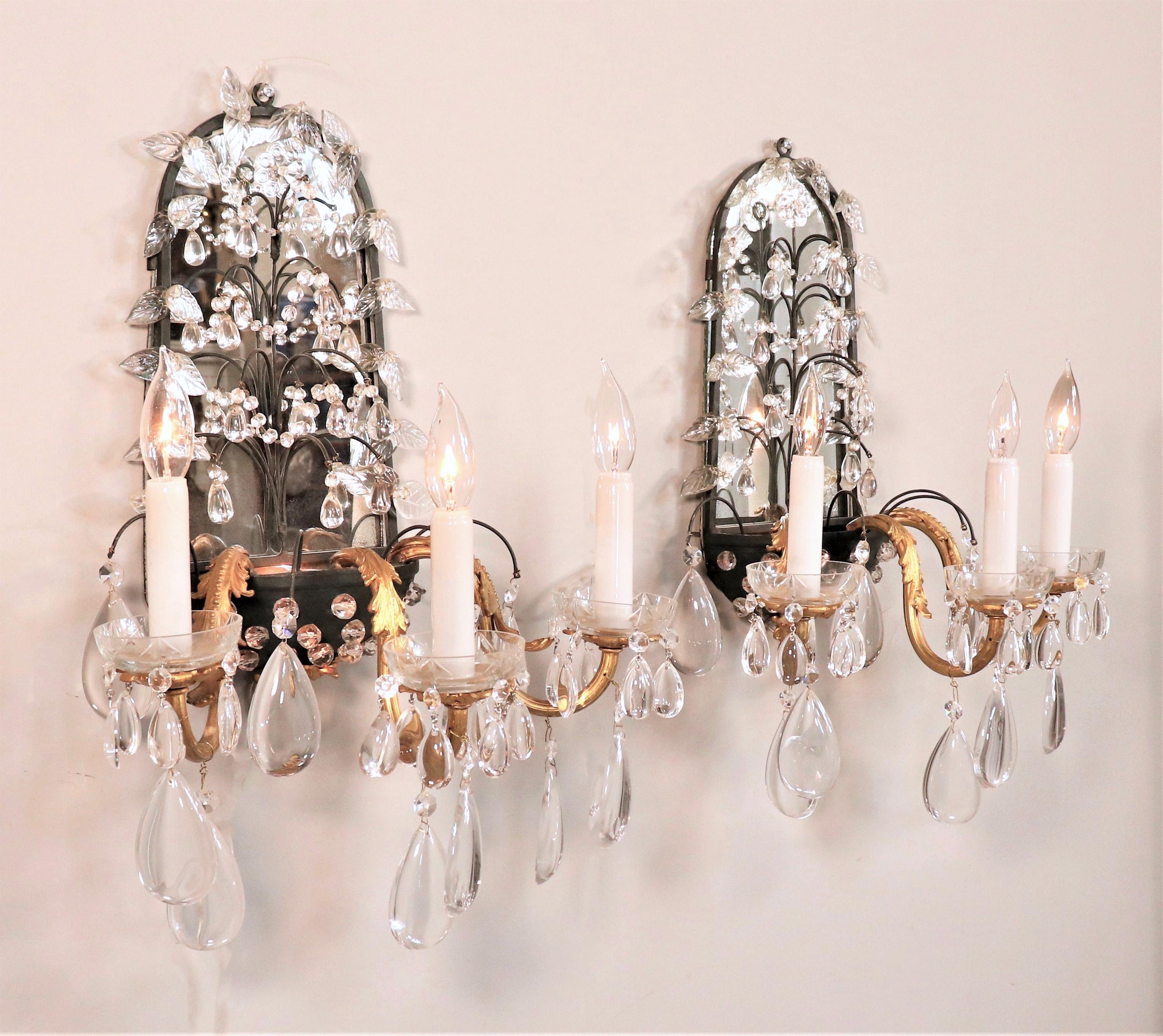This glamorous pair of Louis XV-style sconces is attributed to Maison Baguès. Designed with a tole skeleton base and a mirrored back panel adorned with crystals forming a blossoming fruit tree. The bottom of the sconces consists of a black half