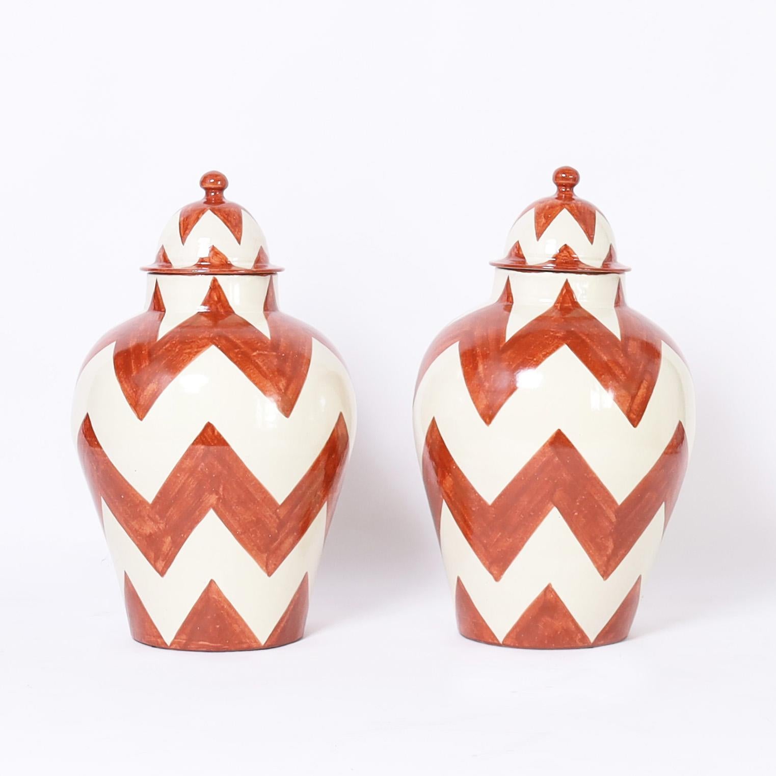 Striking pair of vintage lidded urns handcrafted in terra cotta in classic form and hand decorated in a chevron motif. Signed Mexico on the bottoms.