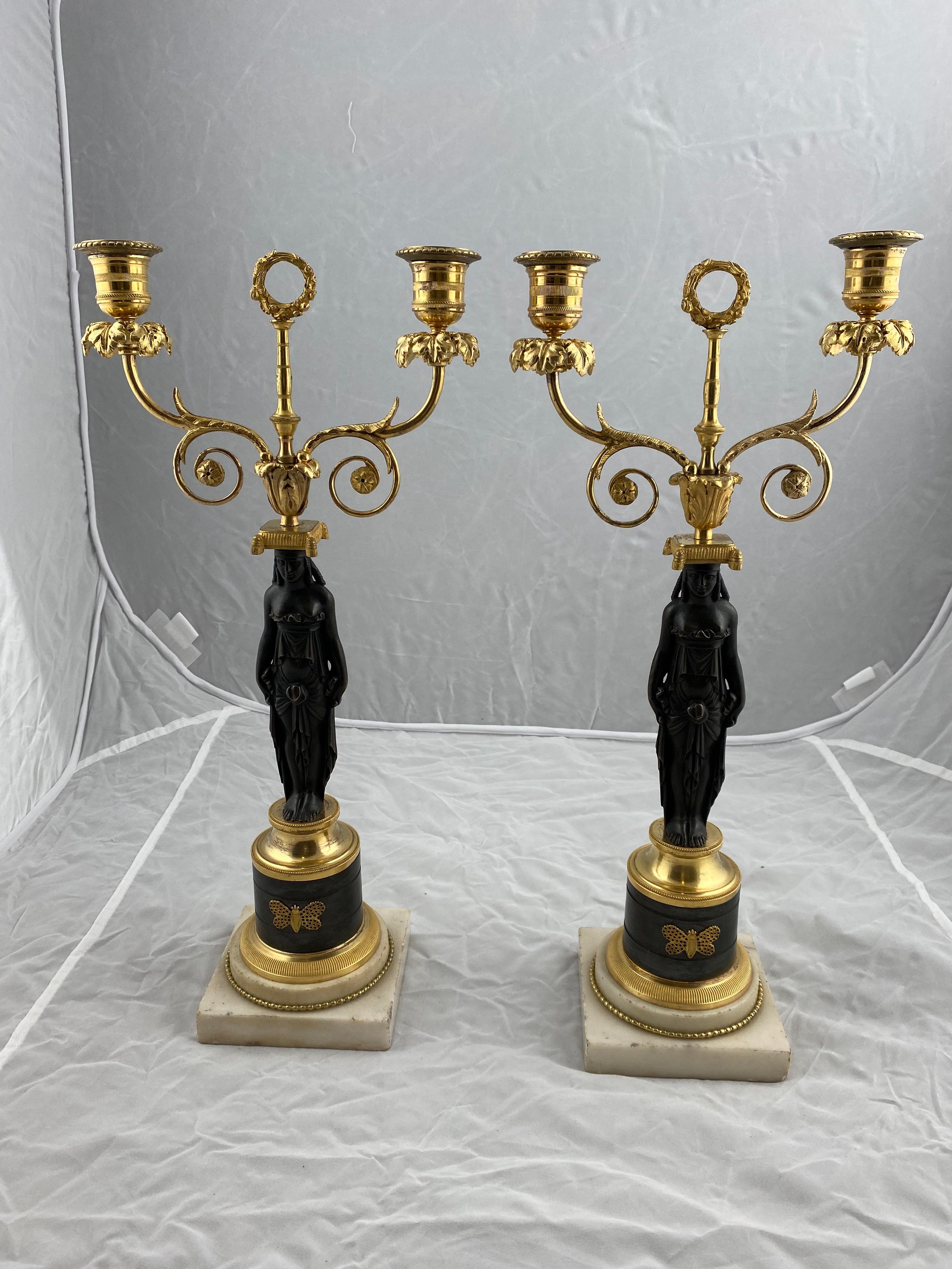 A nice pair of candelabras made for two candles each. Marble bases with dark-adapted columns on which Greek Roman Goddesses stand bearing the candleholders on a cushion on their head.
Unusual design.