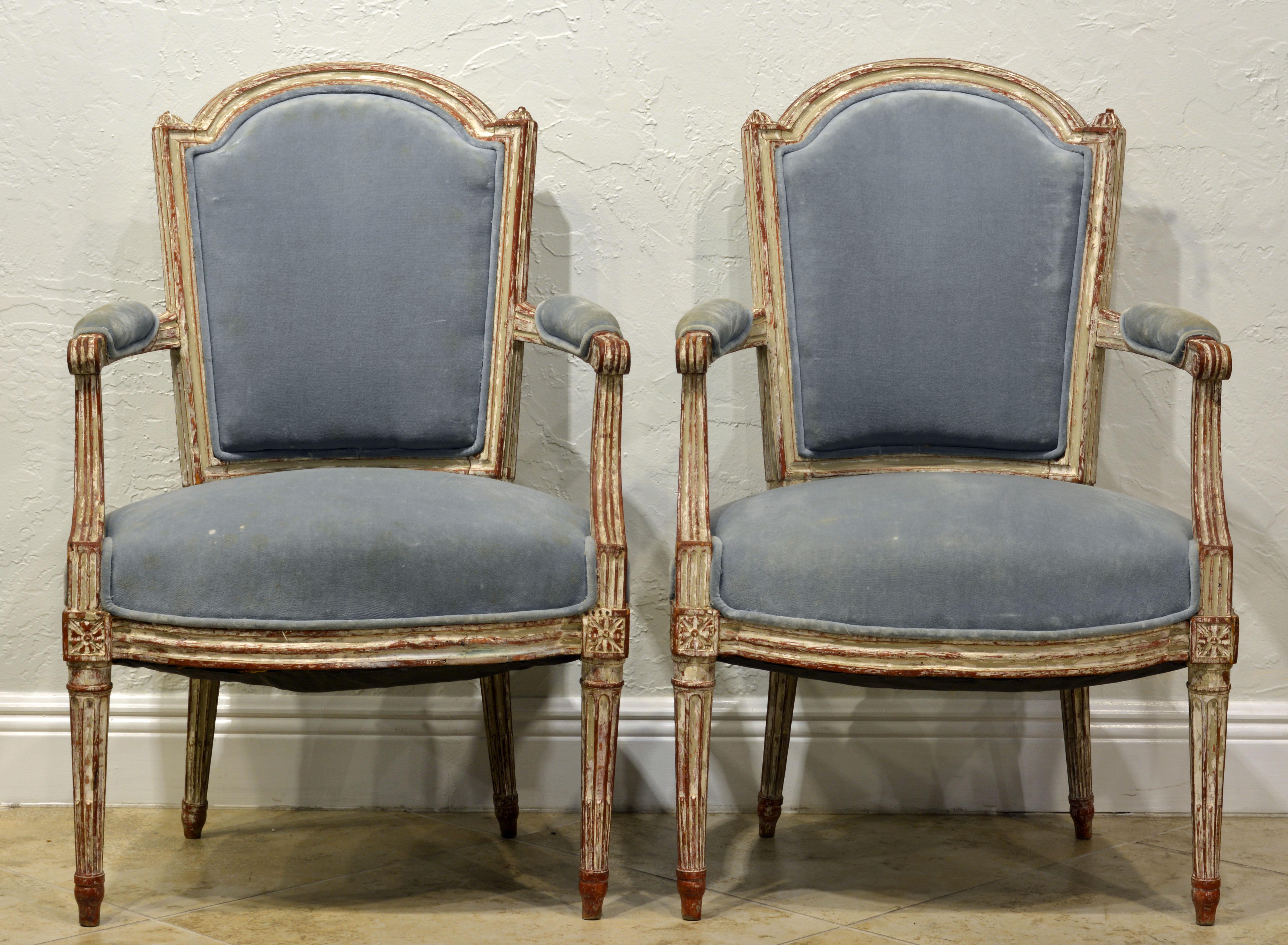 These very attractive French carved and painted armchairs dating to the Louis XVI period feature upholstered seats, armrests and backs in wonderfully detailed painted frames. The whitish paint shows decorative wear exposing underlying layers.