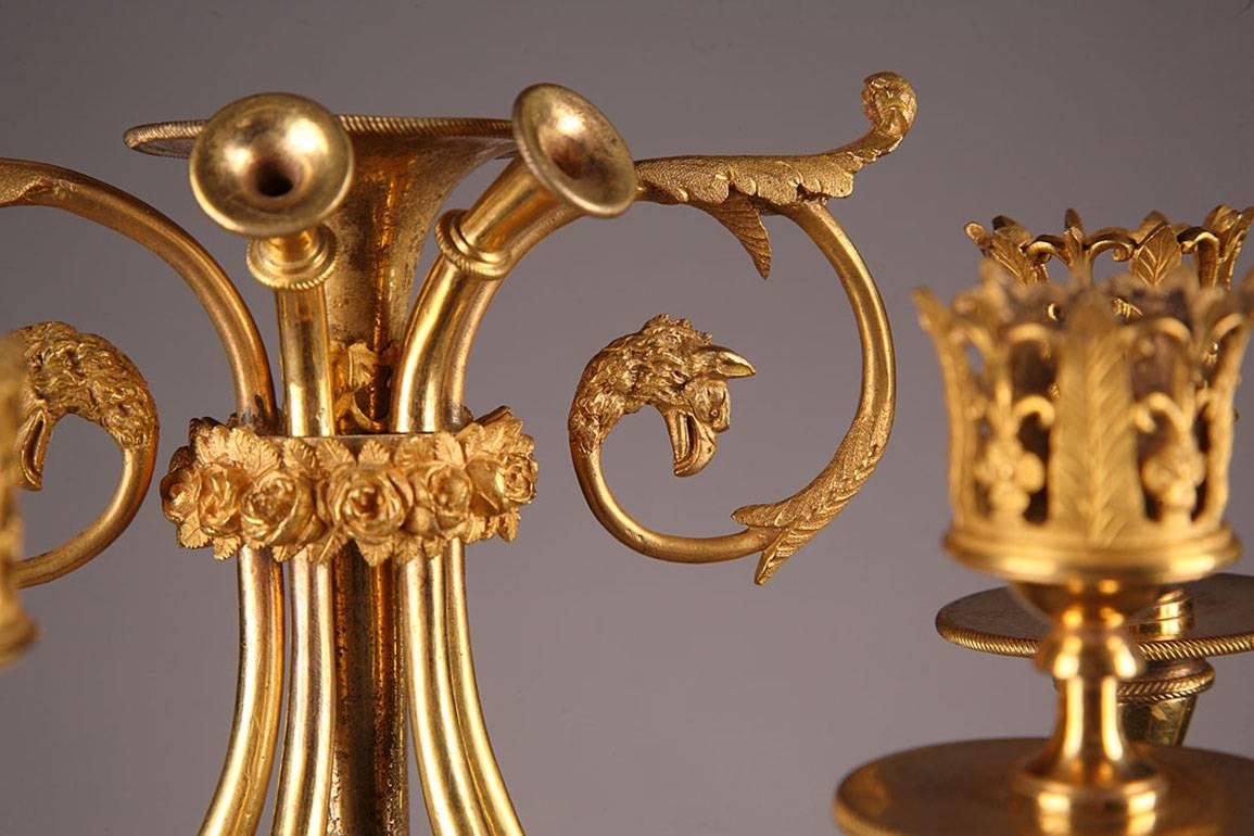 Pair of gilded and sculpted bronze candelabra with four branches each. The branches curve to form trumpets and foliated scrollwork on one end and sockets on the other end. The sockets are intricately embellished with openwork foliage and flowers.