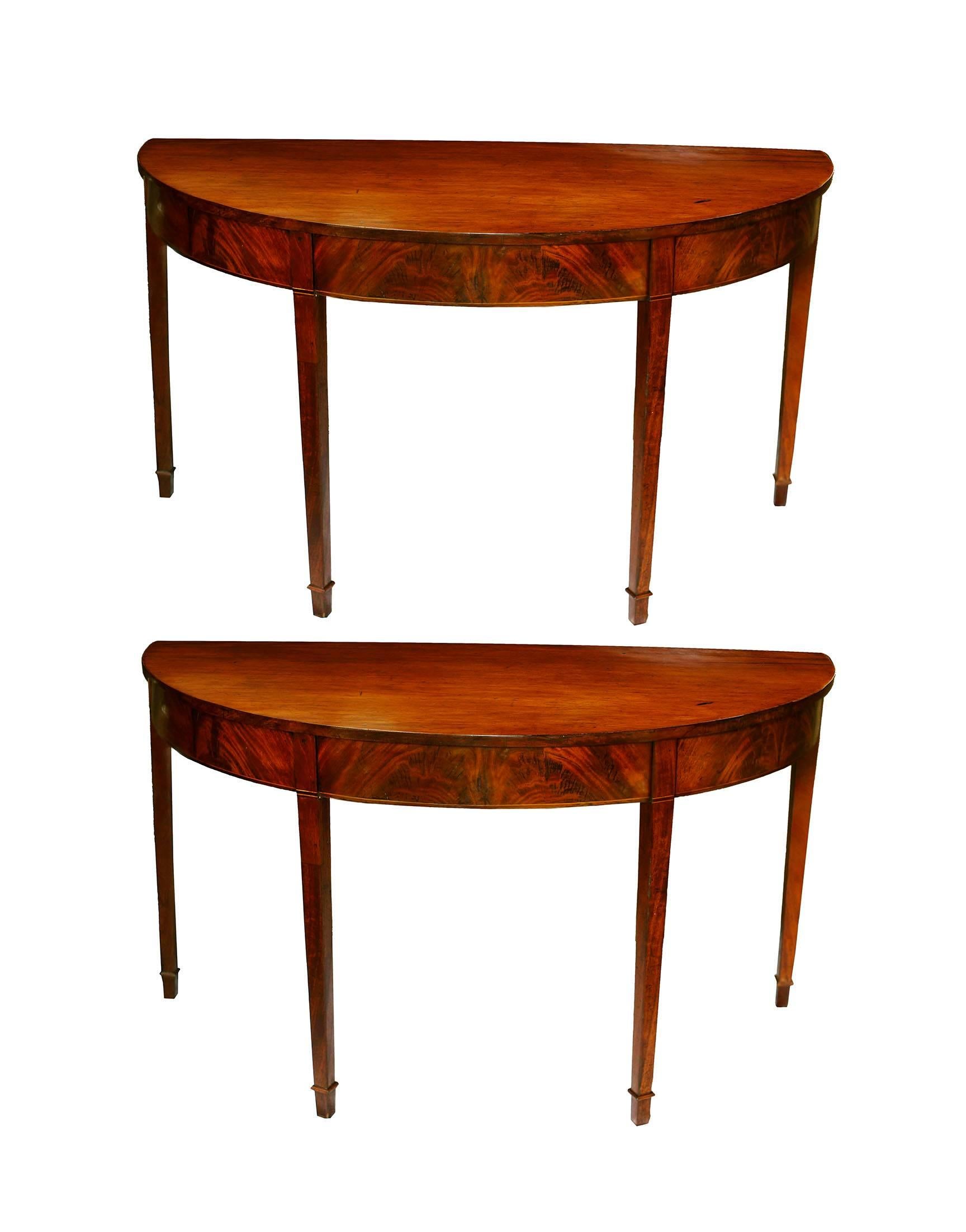 A lovely pair of American console tables in honey colored mahogany. The two demilune feature a graceful elliptical shape with flame mahogany veneer on the frieze and crossbanding of holly and mahogany. The tabletops are composed of single