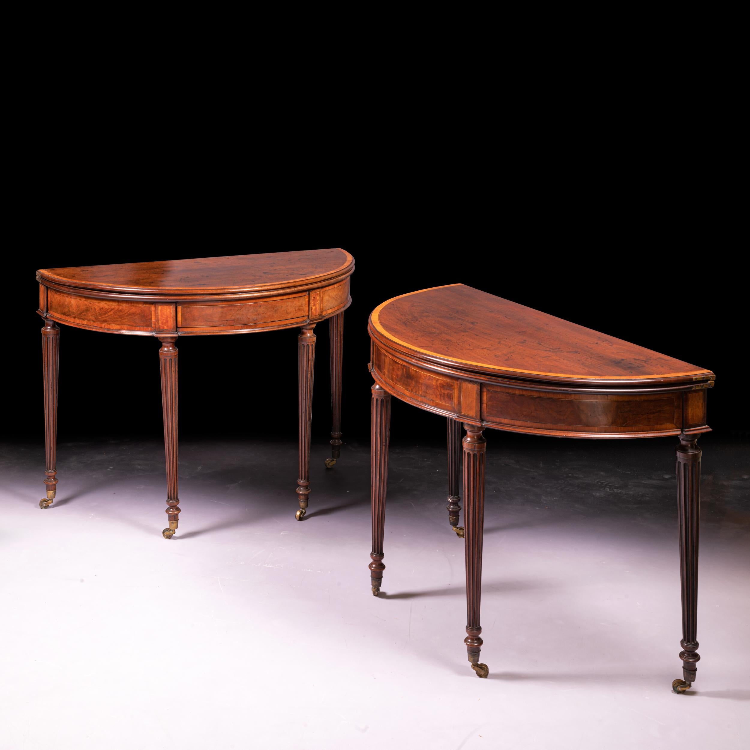 A fine pair of late 18th century Irish George III card tables, constructed in mahogany with crossbanded in satinwood, shaped in demilune outline with moulded frieze and fluted and ring turned tapering legs with brass caps and castors.

Circa