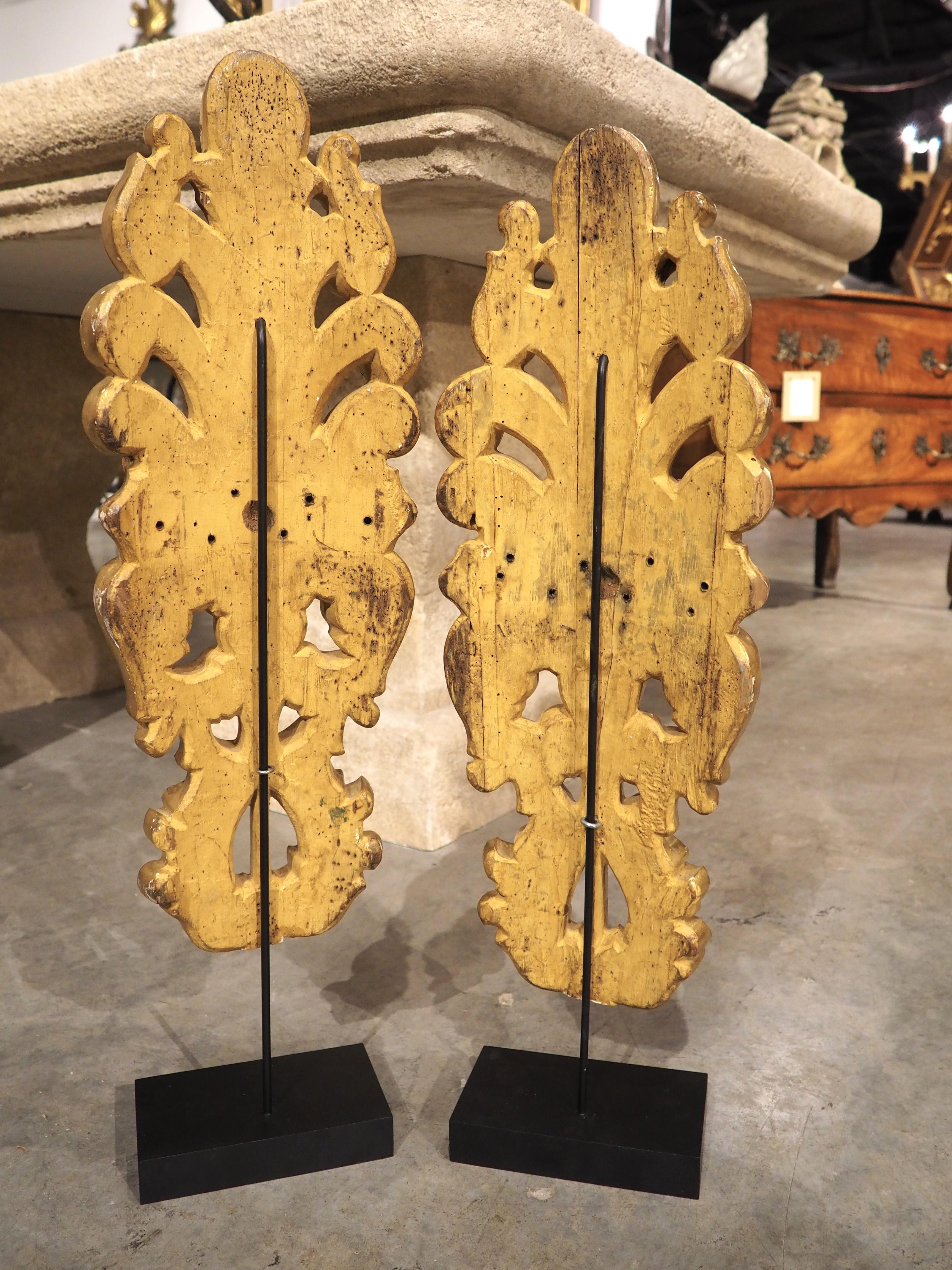This pair of Italian giltwood ornaments are fragments from an original late 1700s Neoclassical architectural. They have been mounted more recently on painted black stands with metal arms.

The gilding has retained much of its original luster,