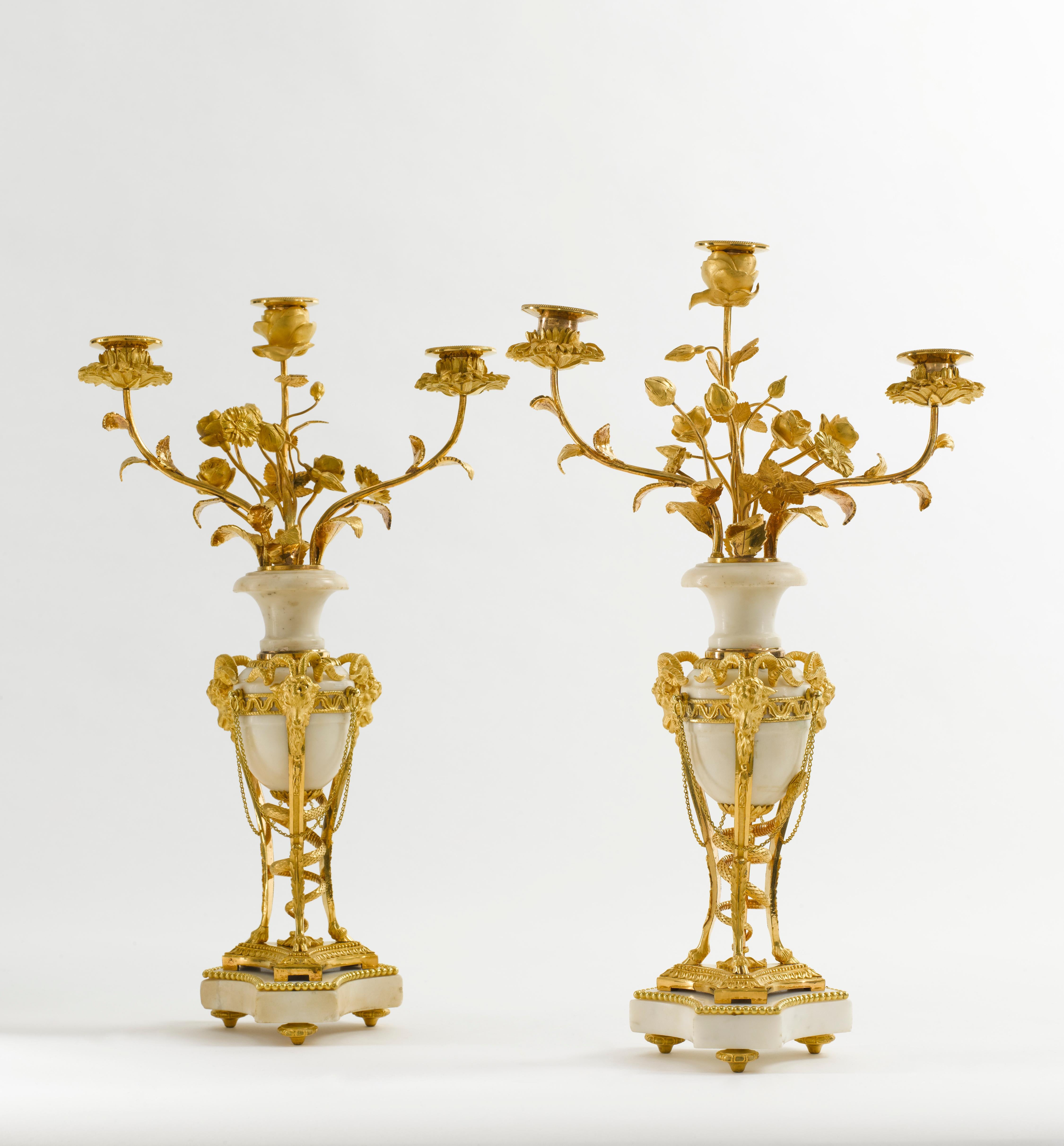 Bella coppia di candelabri Luigi XVI in marmo bianco e bronzo dorato a forma di atene. Il tripode a testa di ariete ha un serpente intrecciato attraverso il gambo, il corpo centrale di forma ovoidale in marmo bianco che emette tre rami foliati, su