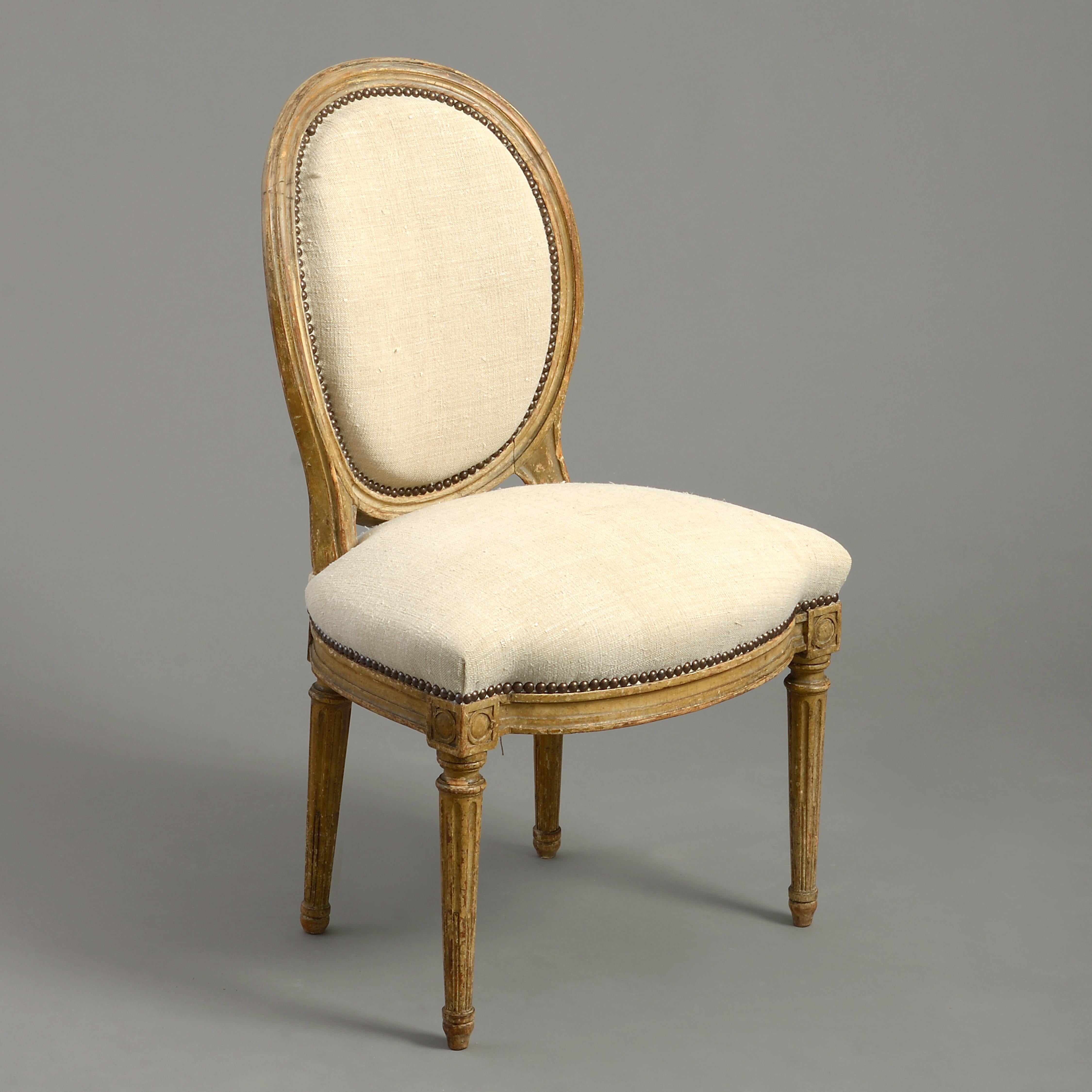 A good pair of late 18th century carved and painted upholstered side chairs, the overstuffed oval backs upon a seat of the safe with close brass nailing. The tapering stop-fluted legs headed by ring paterae.