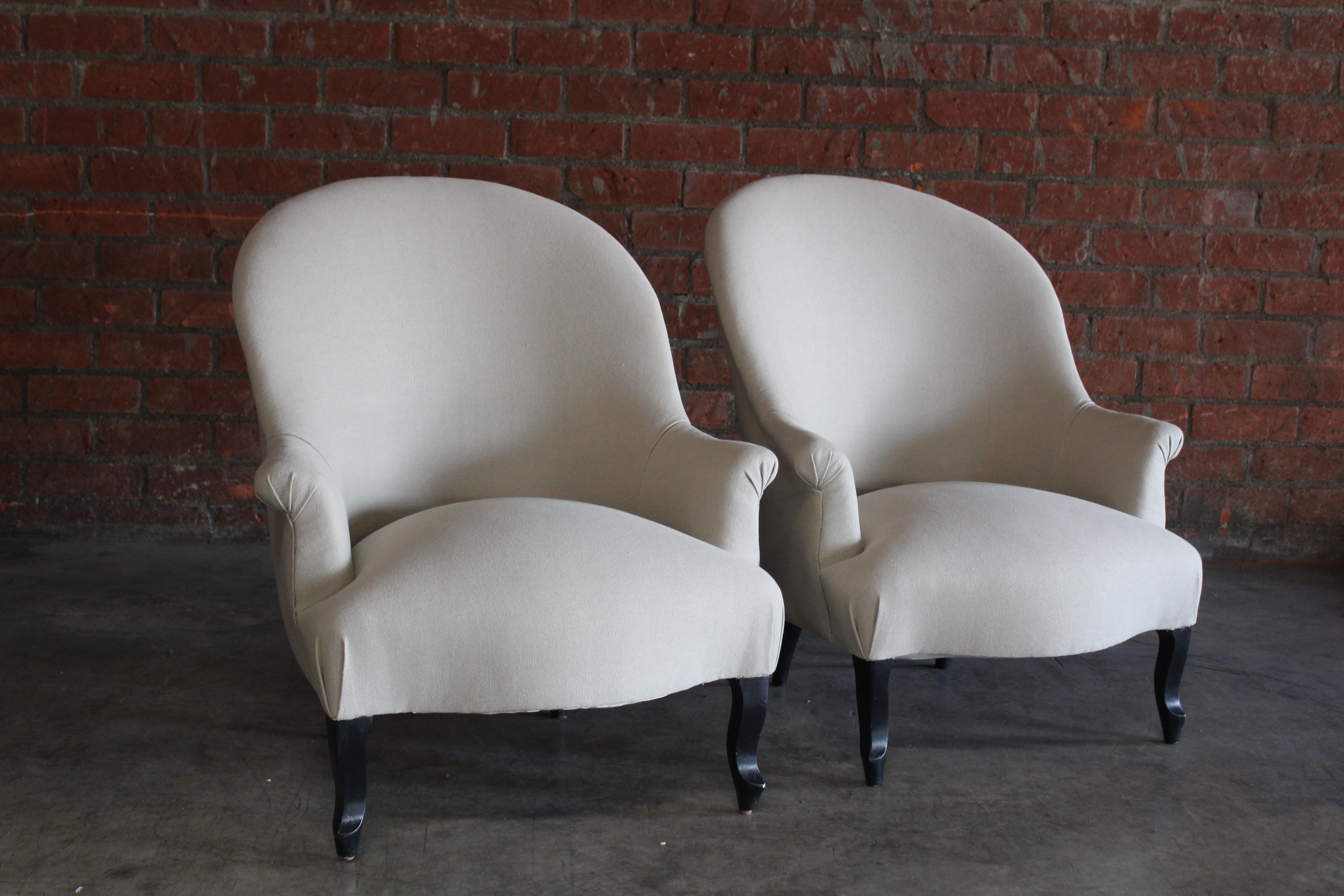 Pair of antique French Napoleon III lounge chairs, late 19th century. The pair have been reupholstered in a beige Belgian linen and restored with new foam and springs. The wooden legs are in their original finish and have been left as is which show