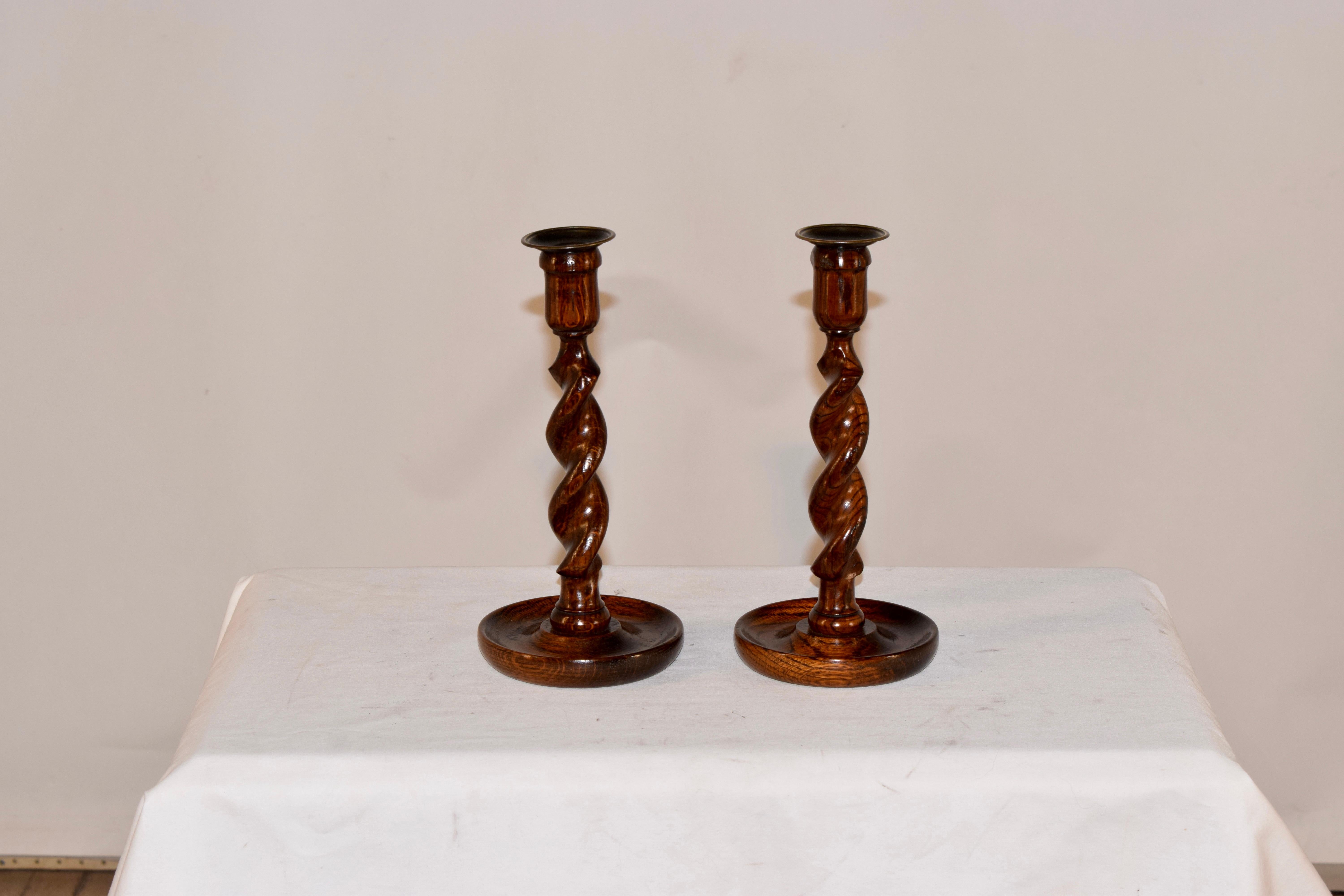 Pair of late 19th century oak candlesticks from England. The candle cups are made from hand cast brass, and are supported on a hand turned barley twist stem, resting on a turned dish shaped base.