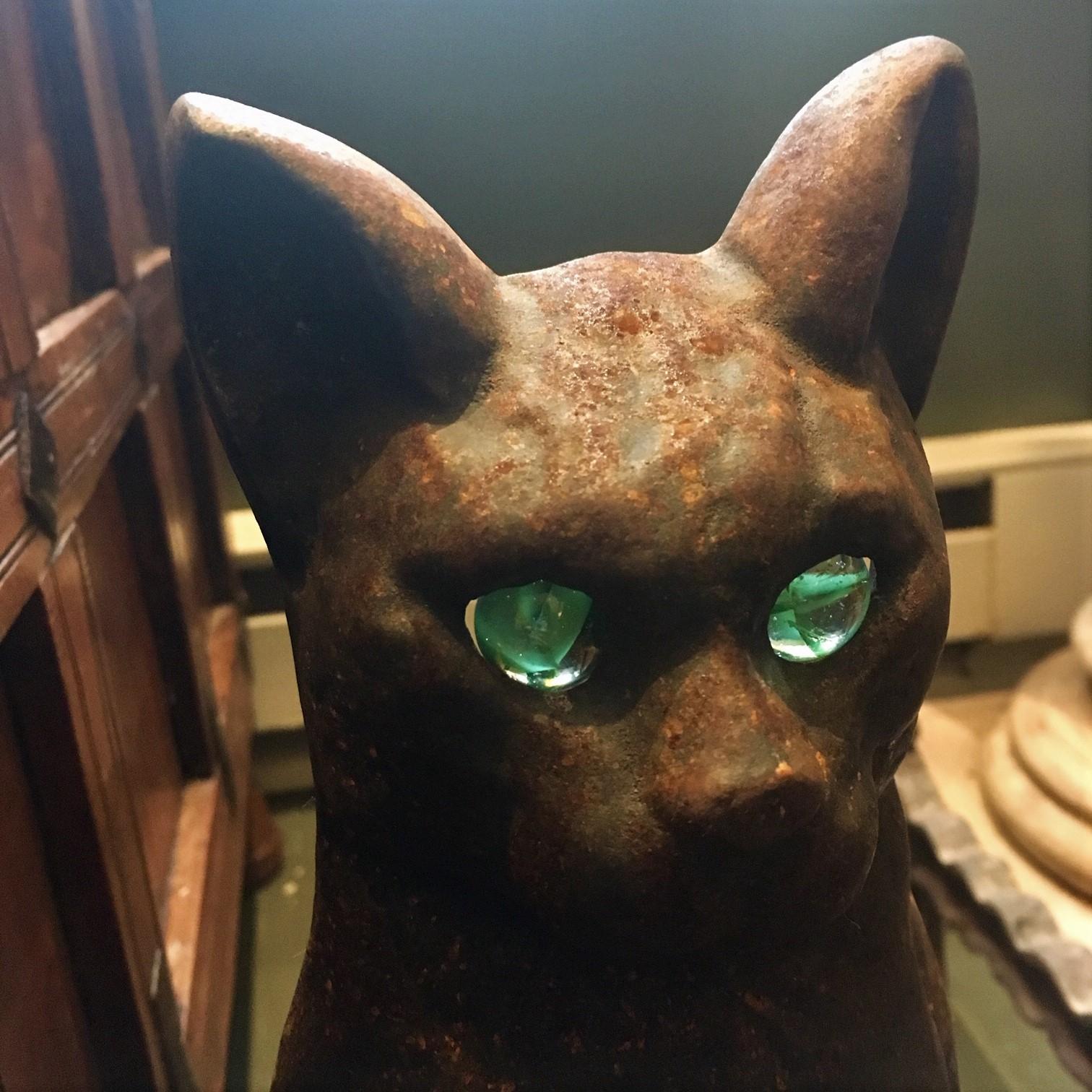 Pair of late 19th century cast iron cat andirons with light, translucent green glass eyes. The proud cats (Siamese?) sit upright on bracket bases, with log supports fitting into keystone dovetails on the back. Not signed, but method of manufacture