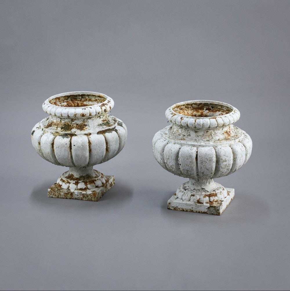 Pair of good sized late 19th century cast iron urns, layers of crusty white paint. France Circa 1890.