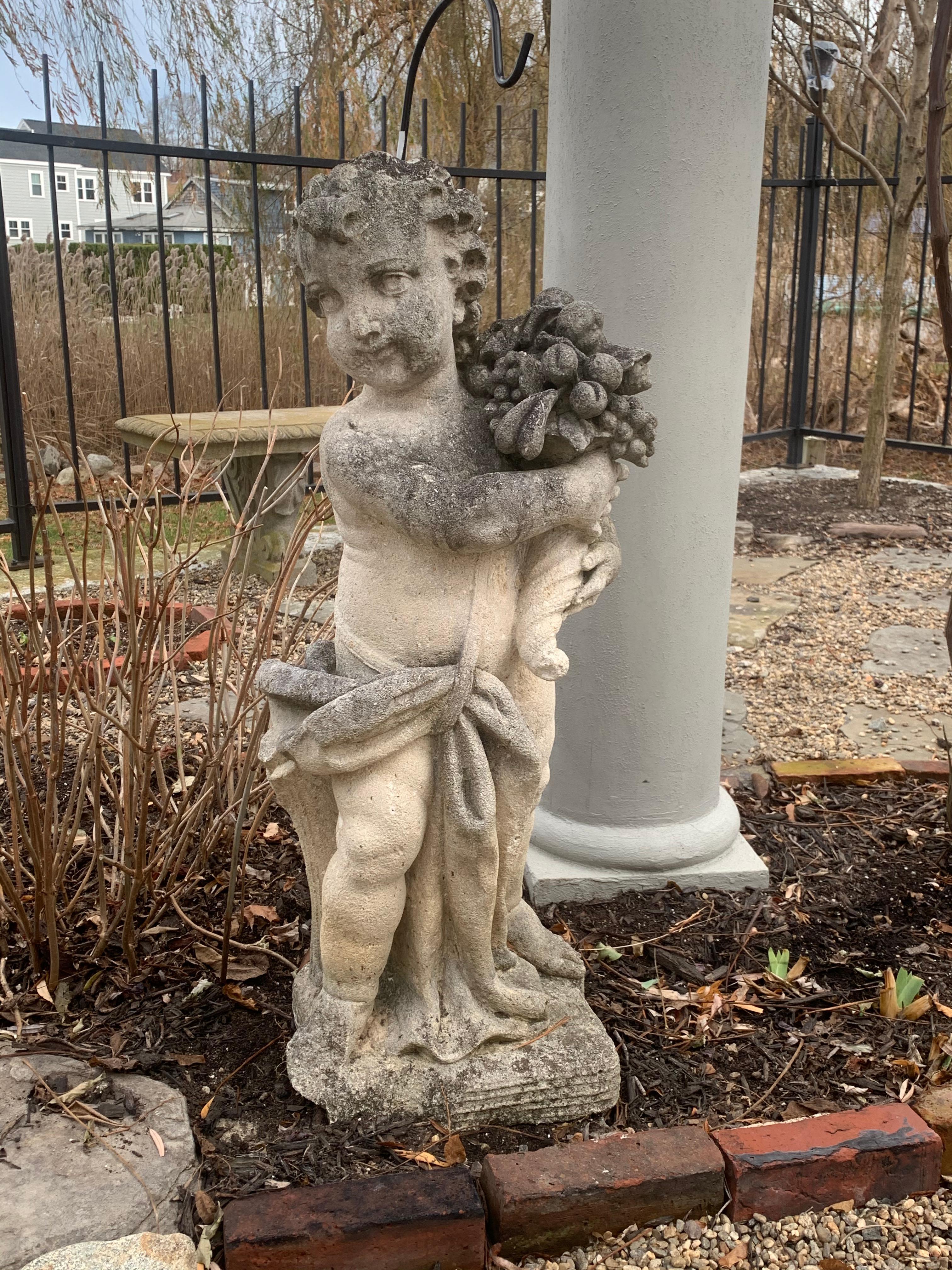 Pair of late 19th to early 20th century cast stone statues or children or putti. One holding a basket of flowers, one holding a cornucopia. Each is a beautiful sandstone with lichen and patina.