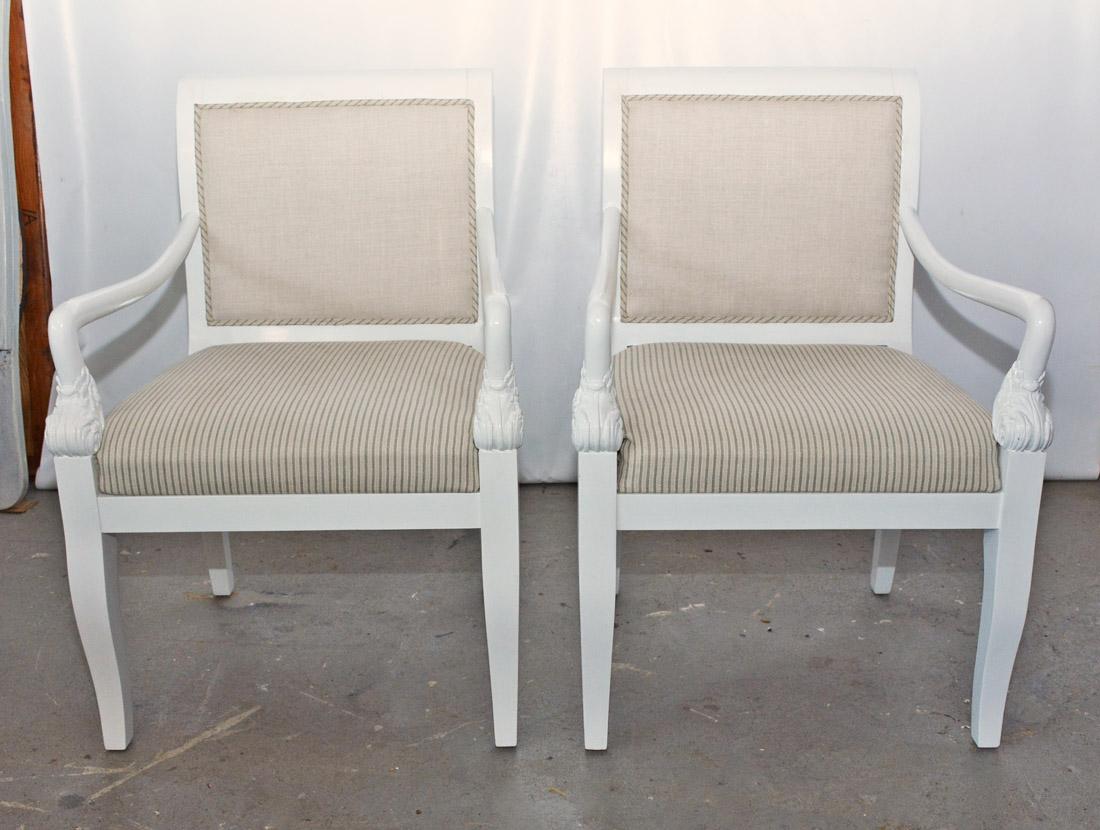 The pair of late 19th century lounge chairs are in the Empire style. The curved arms end with carved acanthus leaves. The seats and bordering gimp on the backs are newly upholstered in a green and beige striped linen, while the backs are in a
