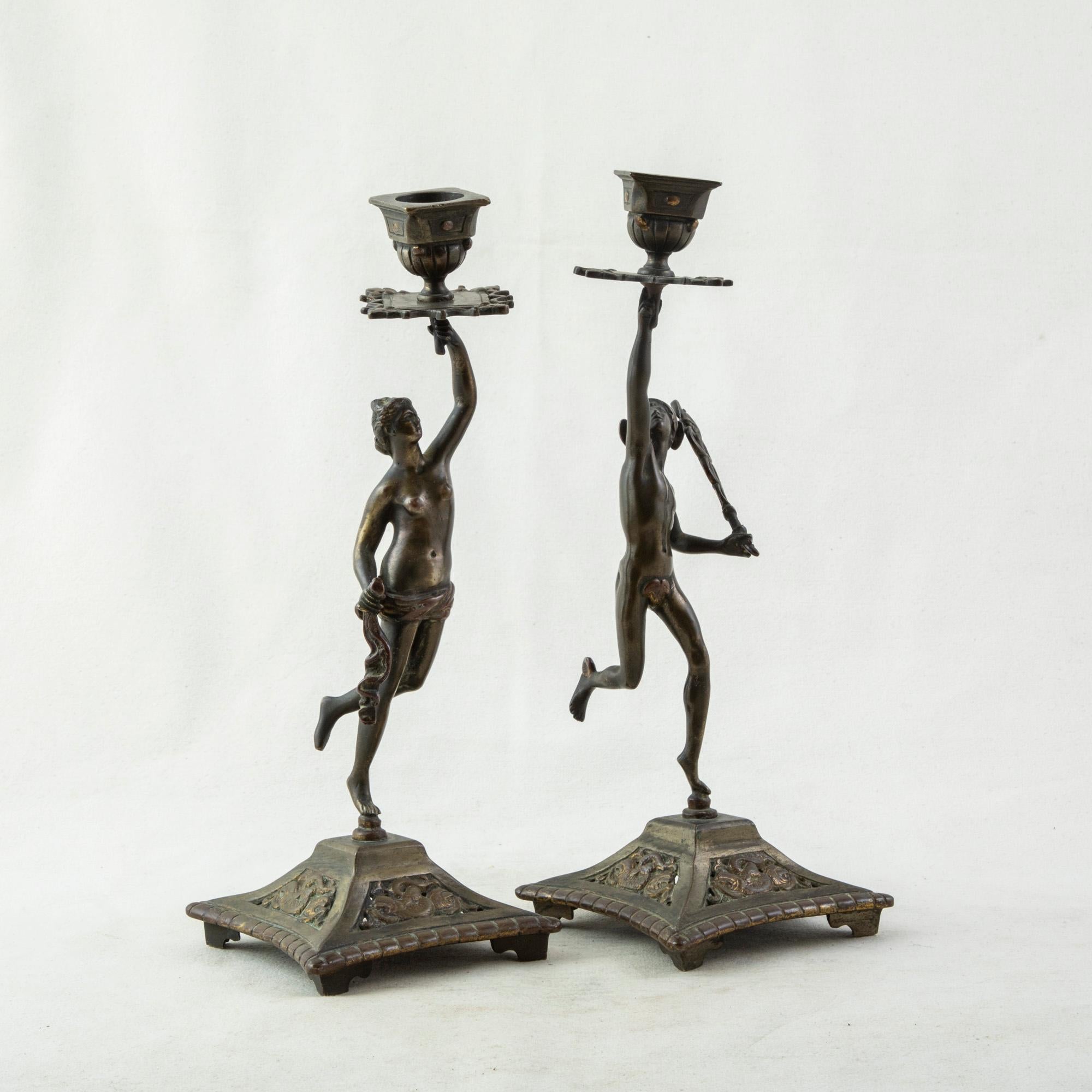 This pair of late nineteenth century bronze candlesticks feature the Roman gods Venus and Mercury each holding aloft the candle holders. Venus, the god of love, stands with a cloth draped around her waist, and Mercury, the messenger god, wears a