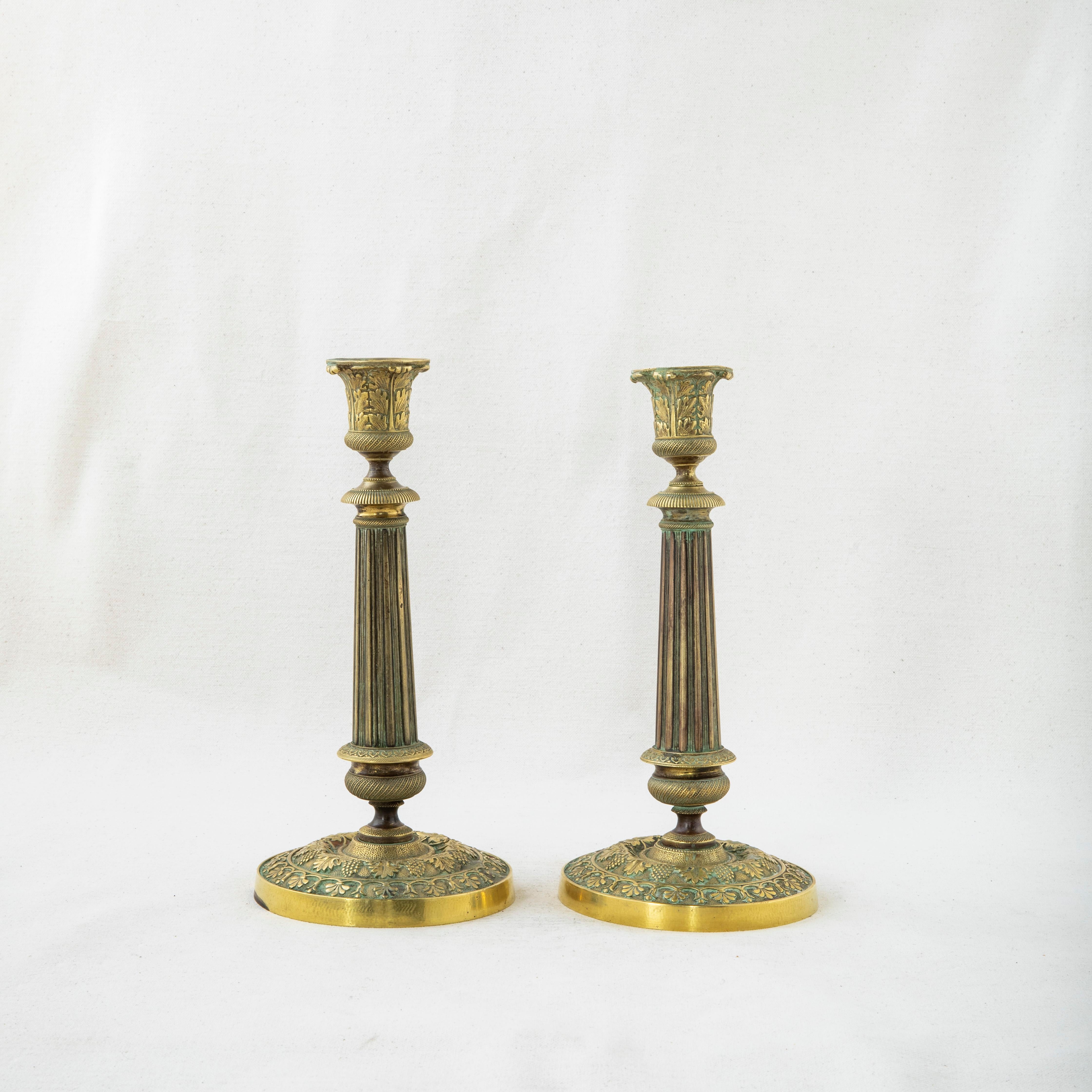This pair of late nineteenth century French bronze candlesticks features a grape and grape leaf motif and fluting. Each candlestick measures 9.25 inches tall by 4.5 inches in diameter at the base. The candlesticks are fitted with attached bobeches