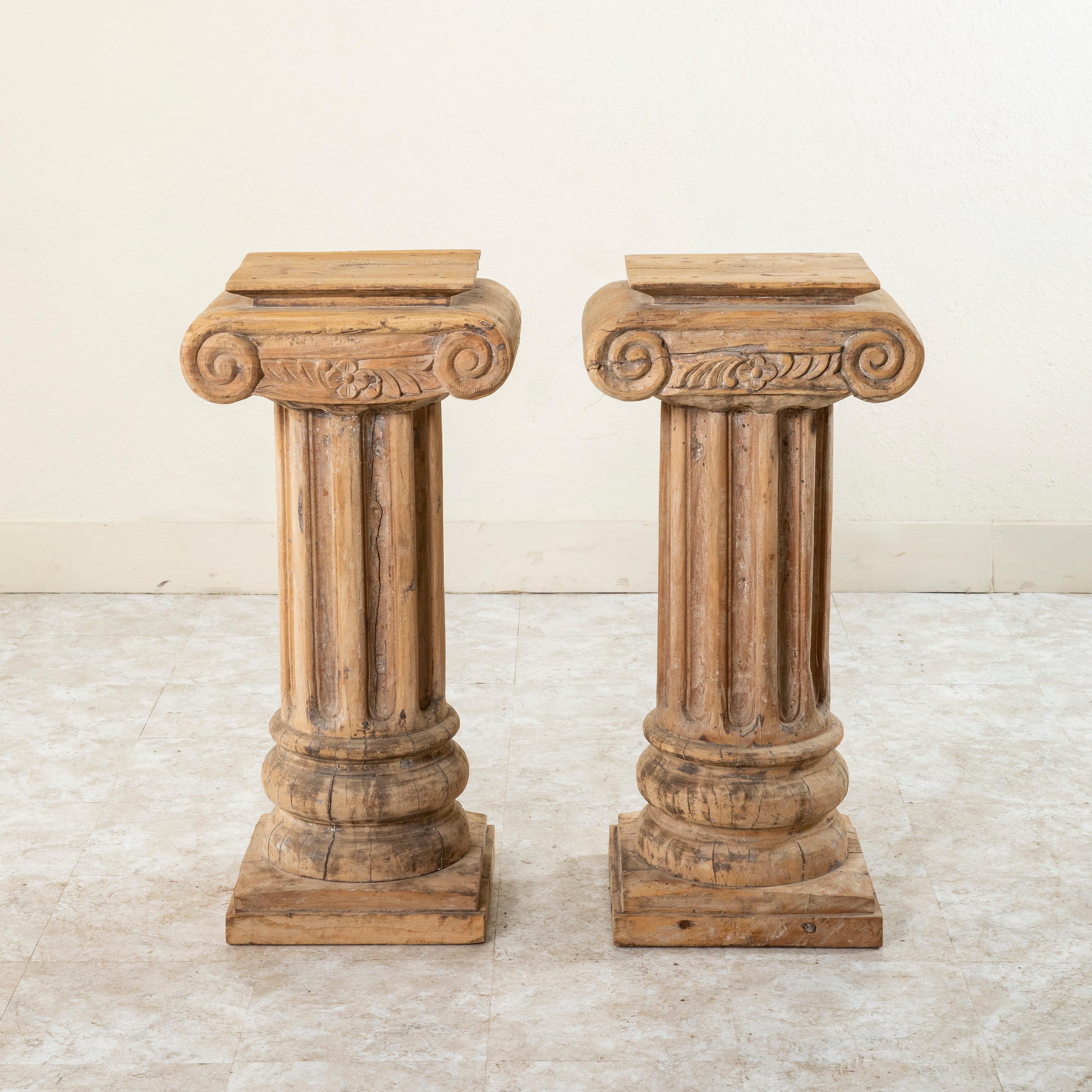 This 35-inch tall pair of large French hand carved beechwood columns or pillars from the late nineteenth century features scrolled ionic capitals detailed with a carved central flower flanked by stylized leaves. Their central fluted pillars rest on